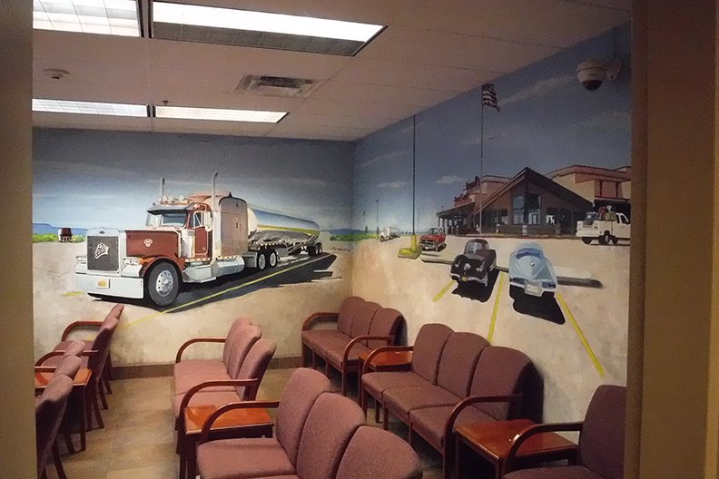 Colorful mural of a parking lot with trucks and cars on the wall behind chairs in a waiting area.