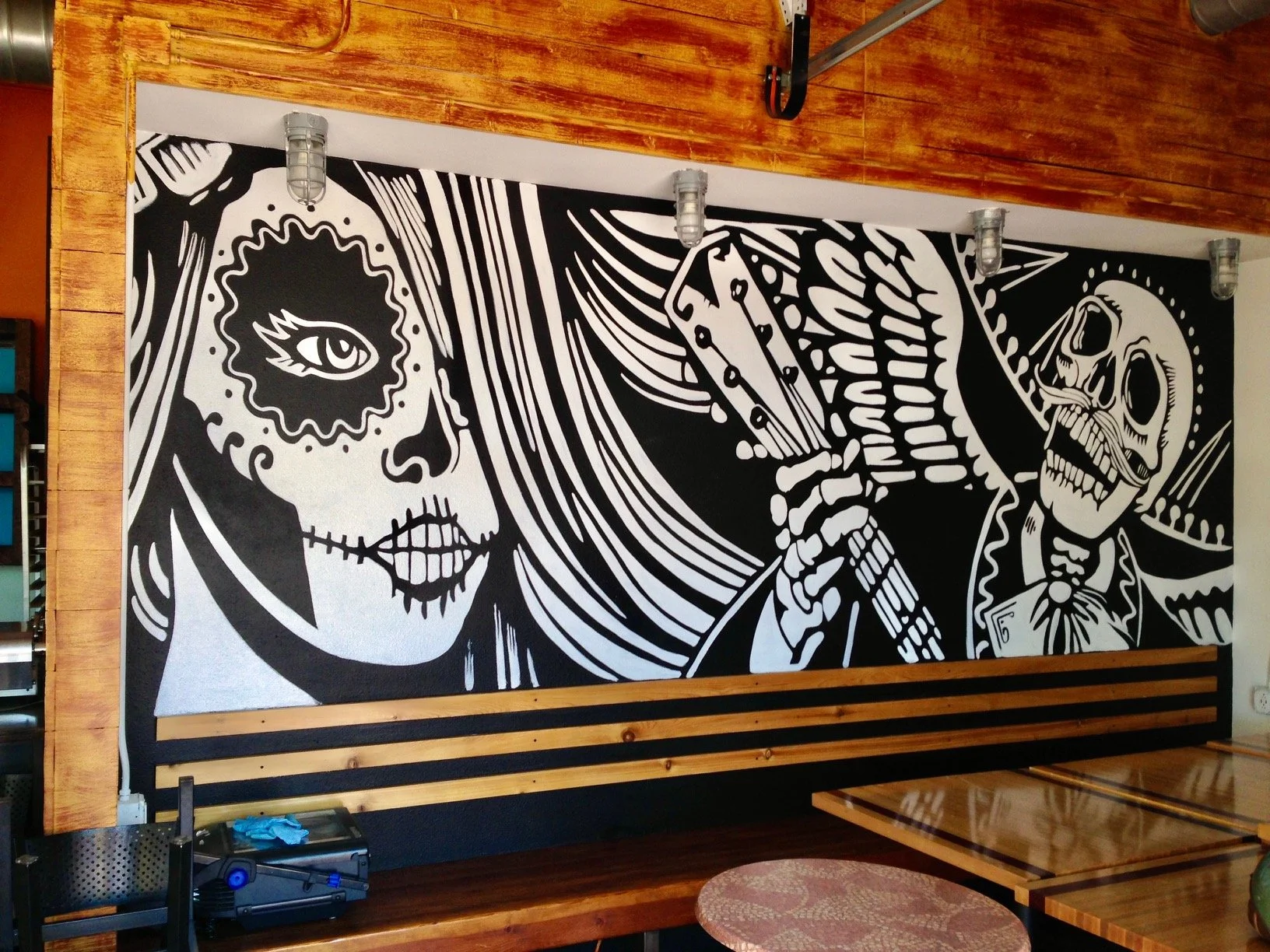 Black and white mural of a Day of the Dead style skull face with a woman and a skeleton holding a card.  Billings, Montana custom art and murals.