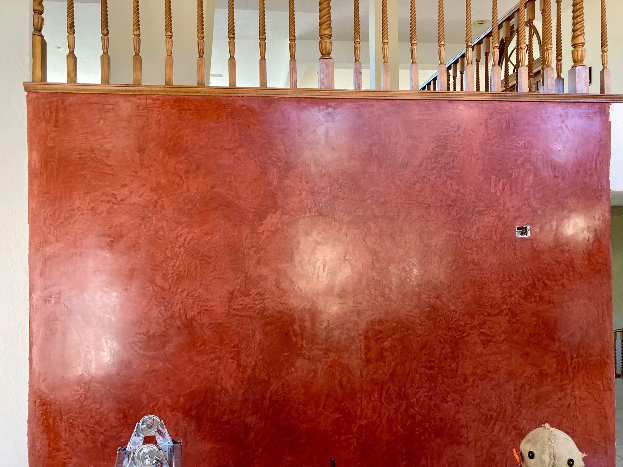 Interior wall with a red textured finish, wooden railing and balusters on the upper level, and a ladder leaning against the wall.