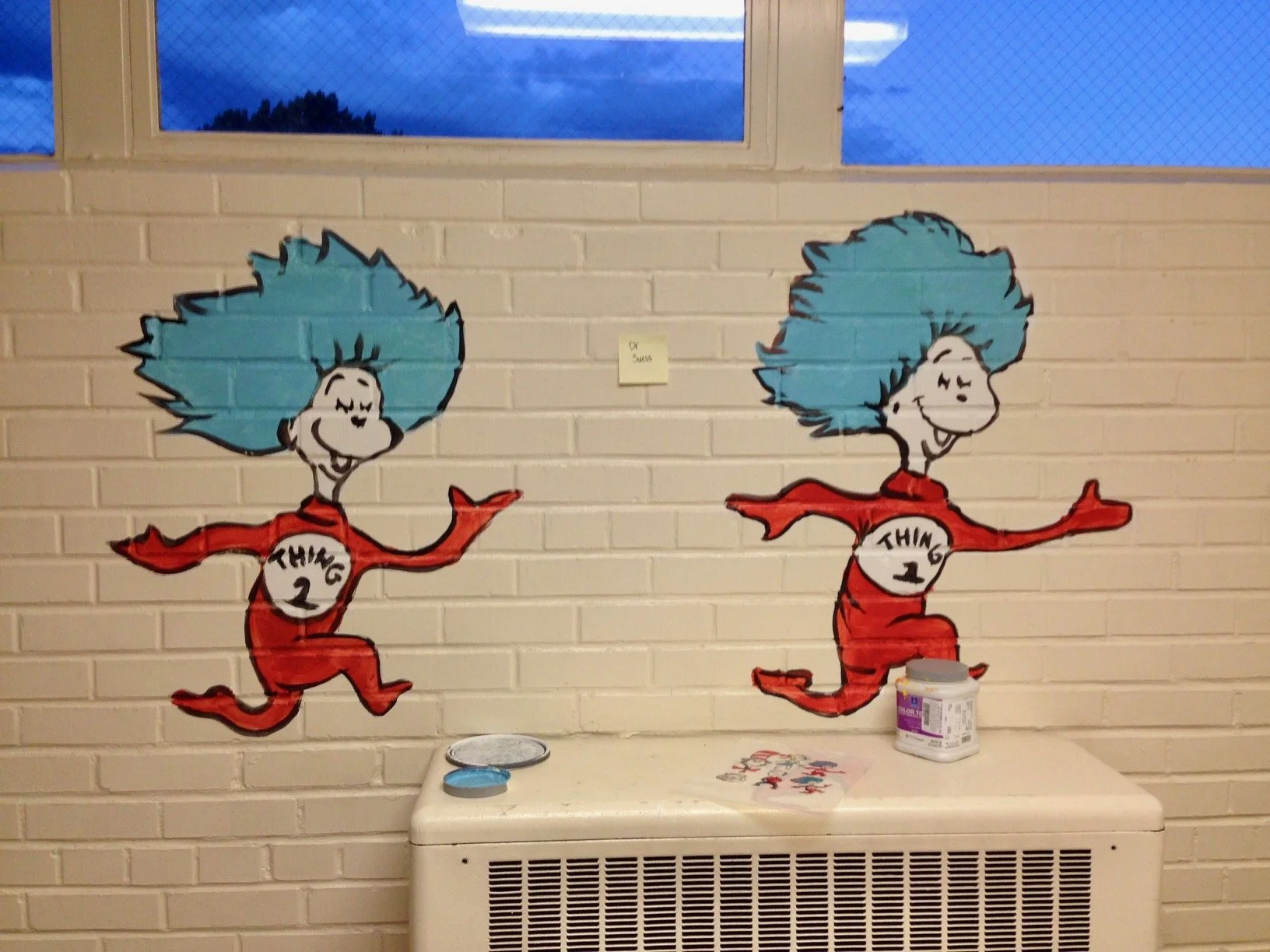 Wall mural of two cartoon characters with blue hair, red outfits, running and smiling, labeled as Thing 1 and Thing 2 from Dr. Seuss, with some graffiti and painting supplies below.