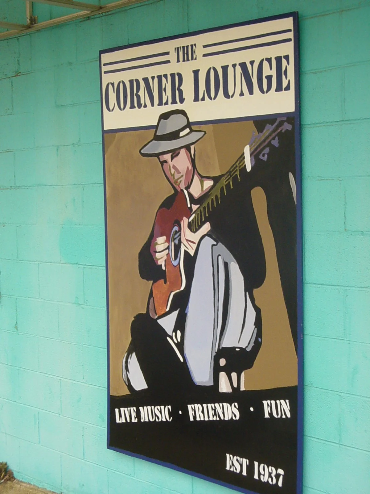 A colorful sign for The Corner Lounge featuring an illustration of a man playing guitar, wearing a hat, with text promoting live music, friends, fun, and established in 1937.