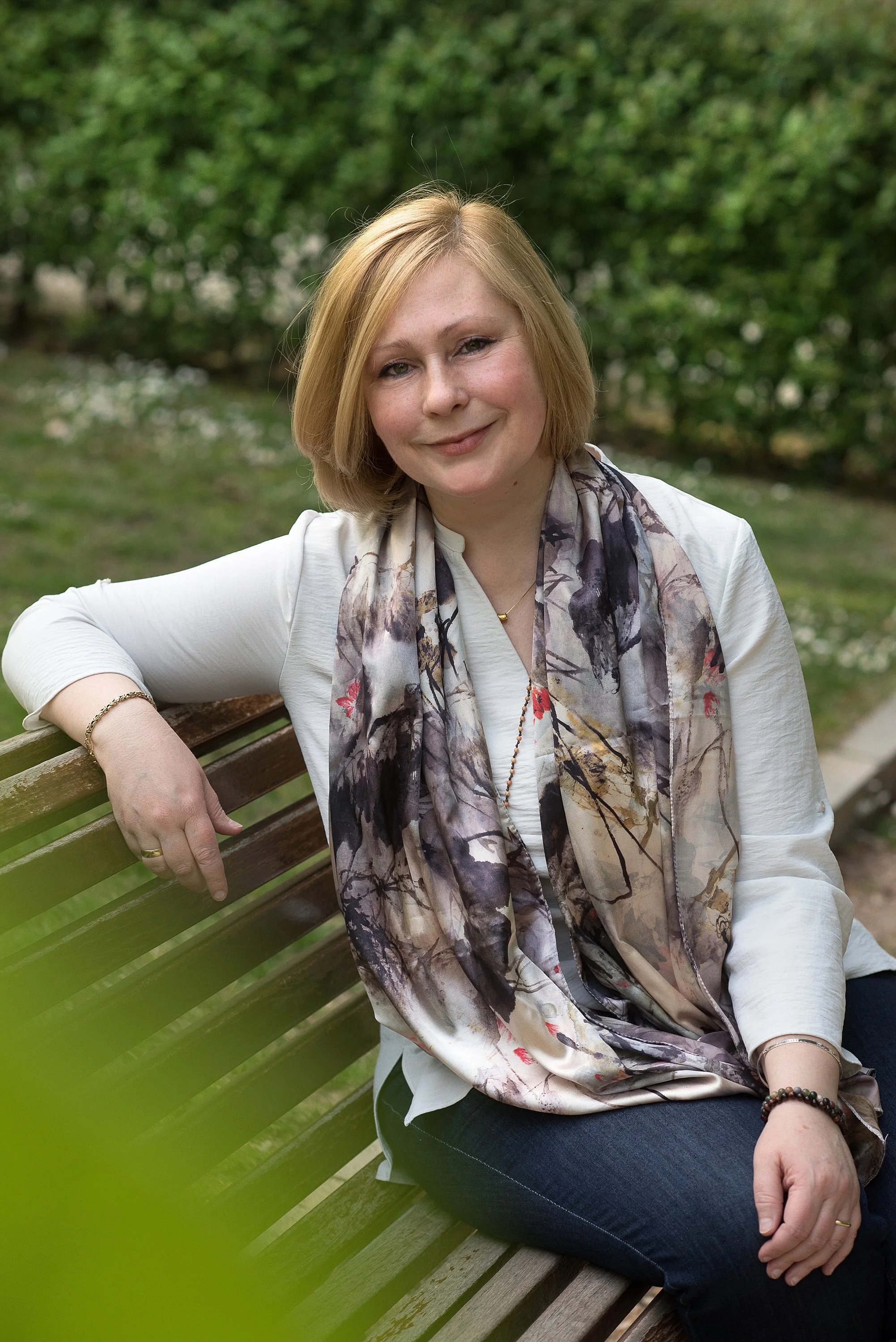 Mujer sonriendo sentada en un banco en un parque con fondo de árboles verdes.