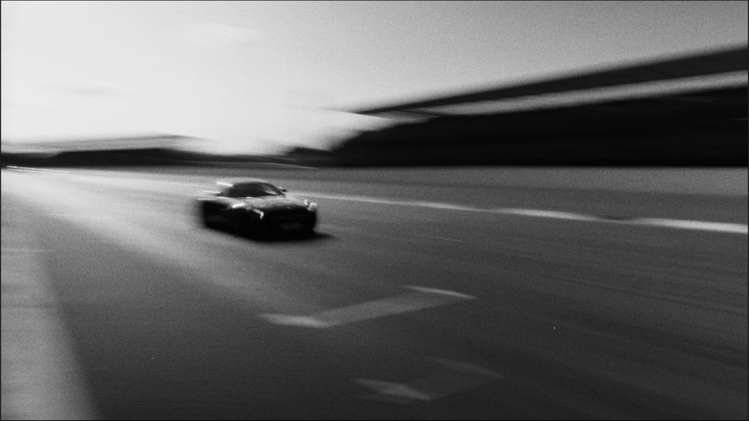 A black sports car driving fast on an open highway with motion blur, in black and white.