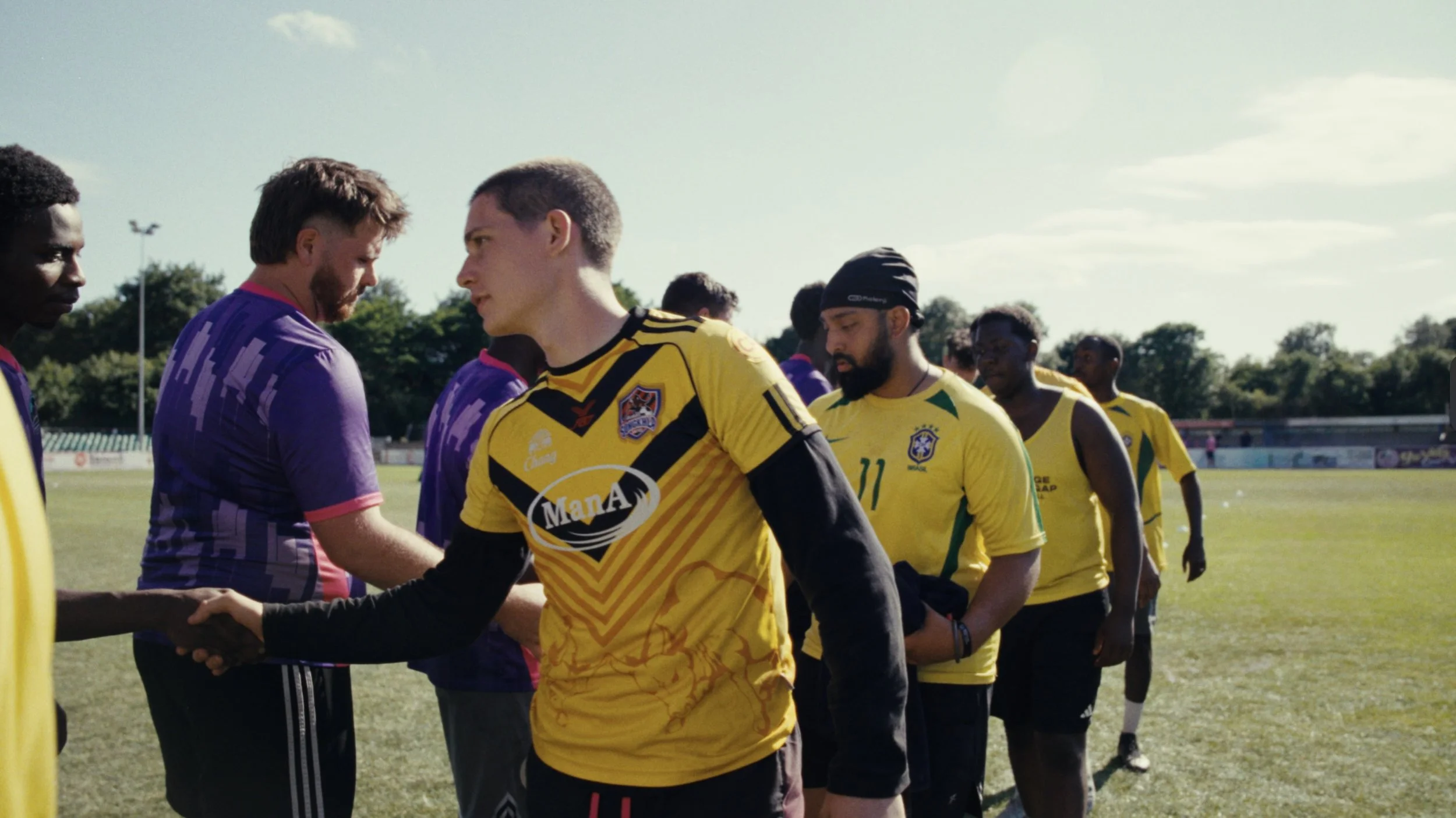 Soccer players shaking hands before a match on a grassy field under a partly cloudy sky.
