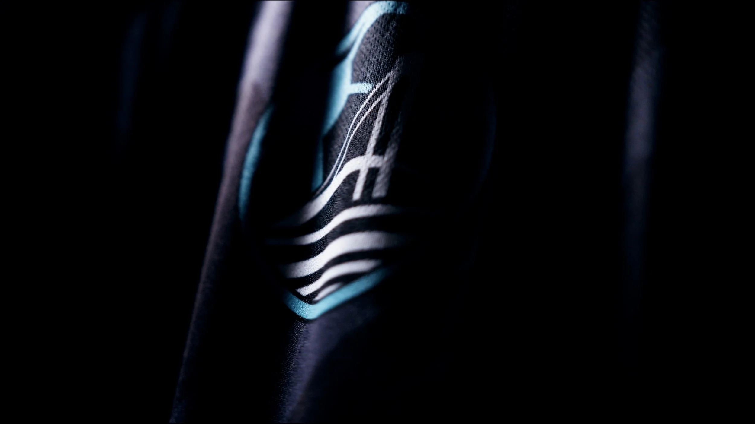 Close-up of a dark fabric with an abstract white and blue logo or design, partially visible.