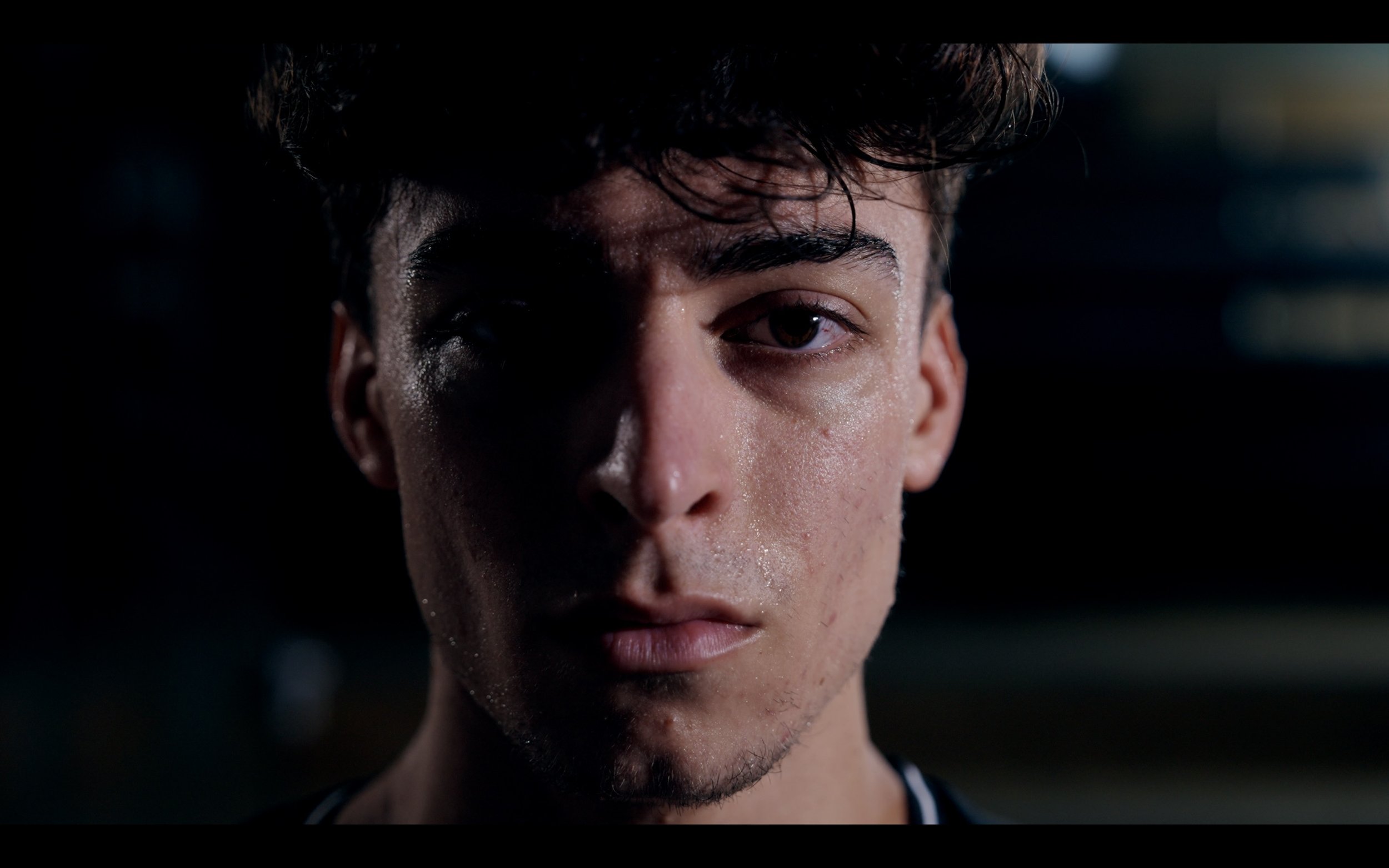 Close-up of a young man's face with wet skin, half in shadow, looking directly at the camera.