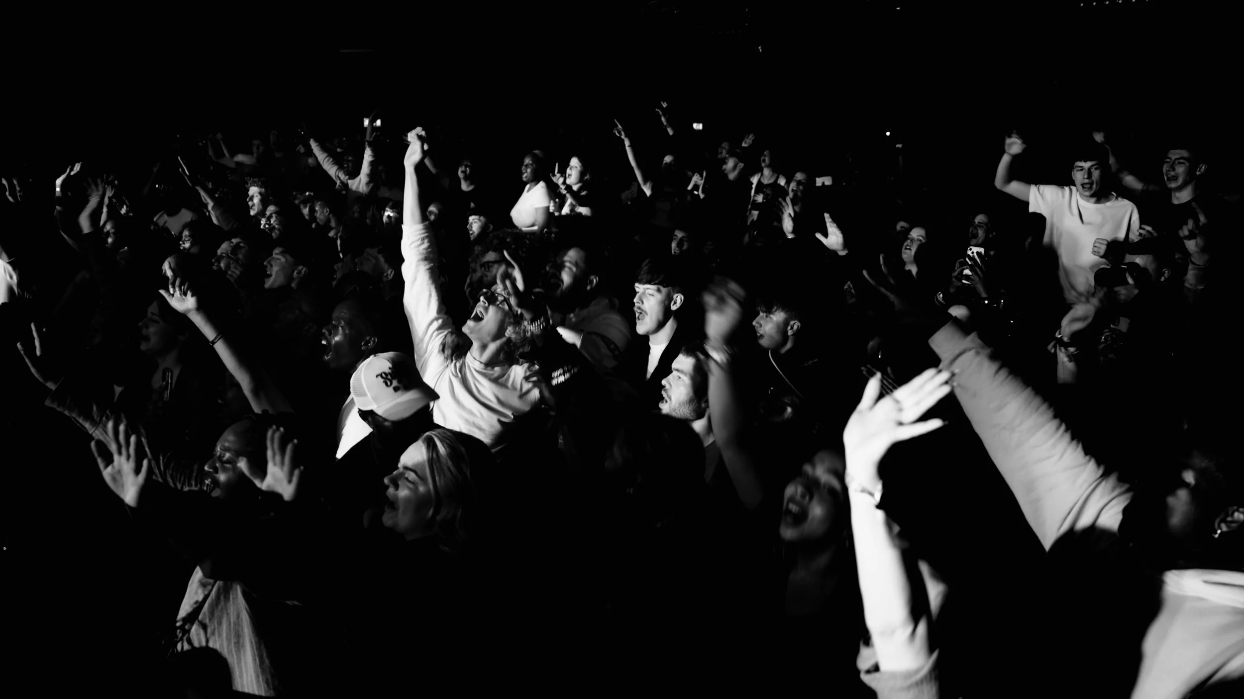 Crowd of people at concert cheering and raising hands, black and white photo.