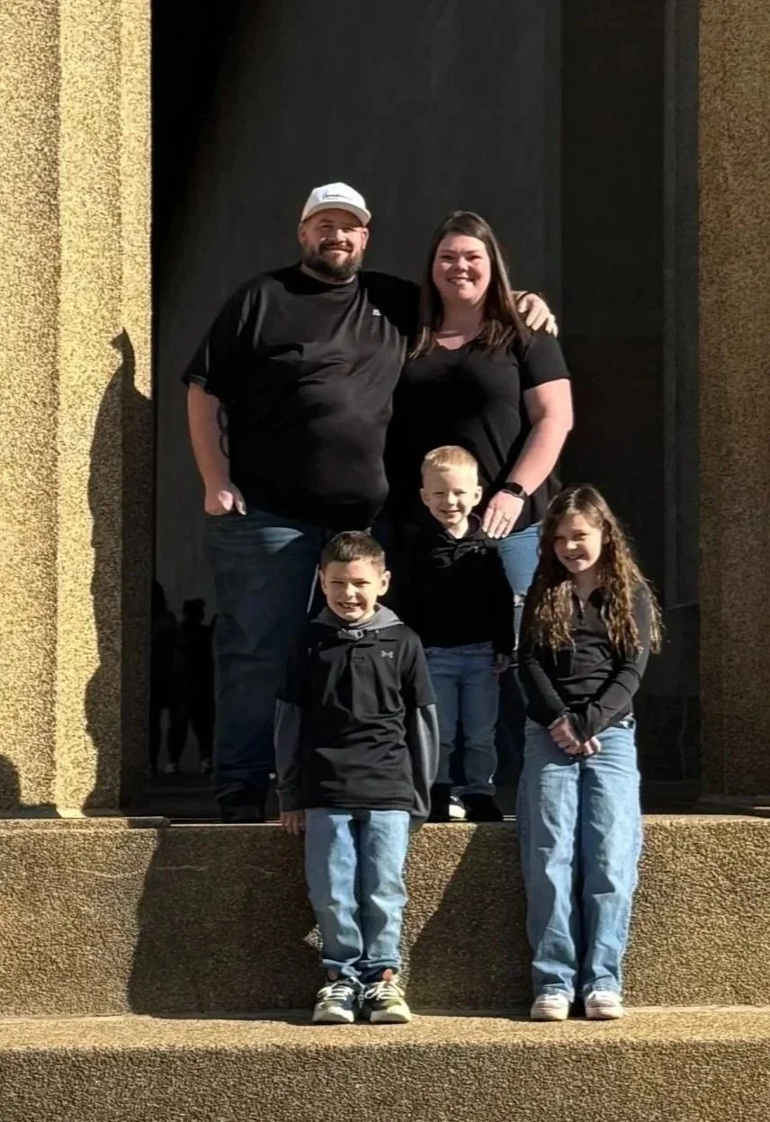 A family photo with two adults and three children standing on steps outside a building.