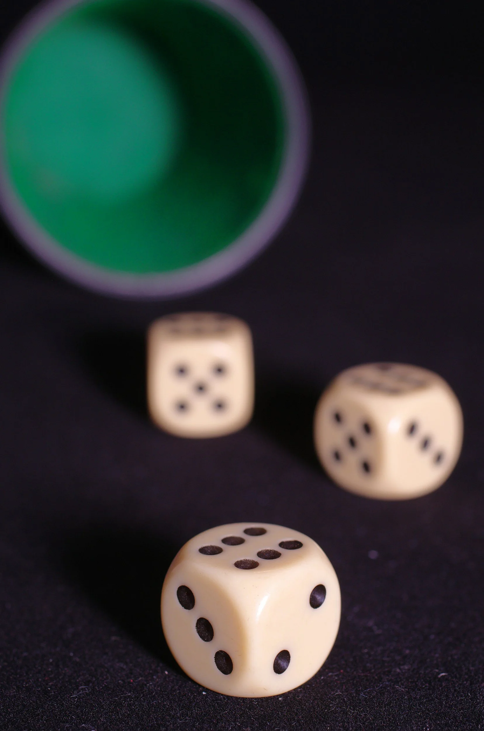 Three dice on a black surface with a green and purple cup in the background.