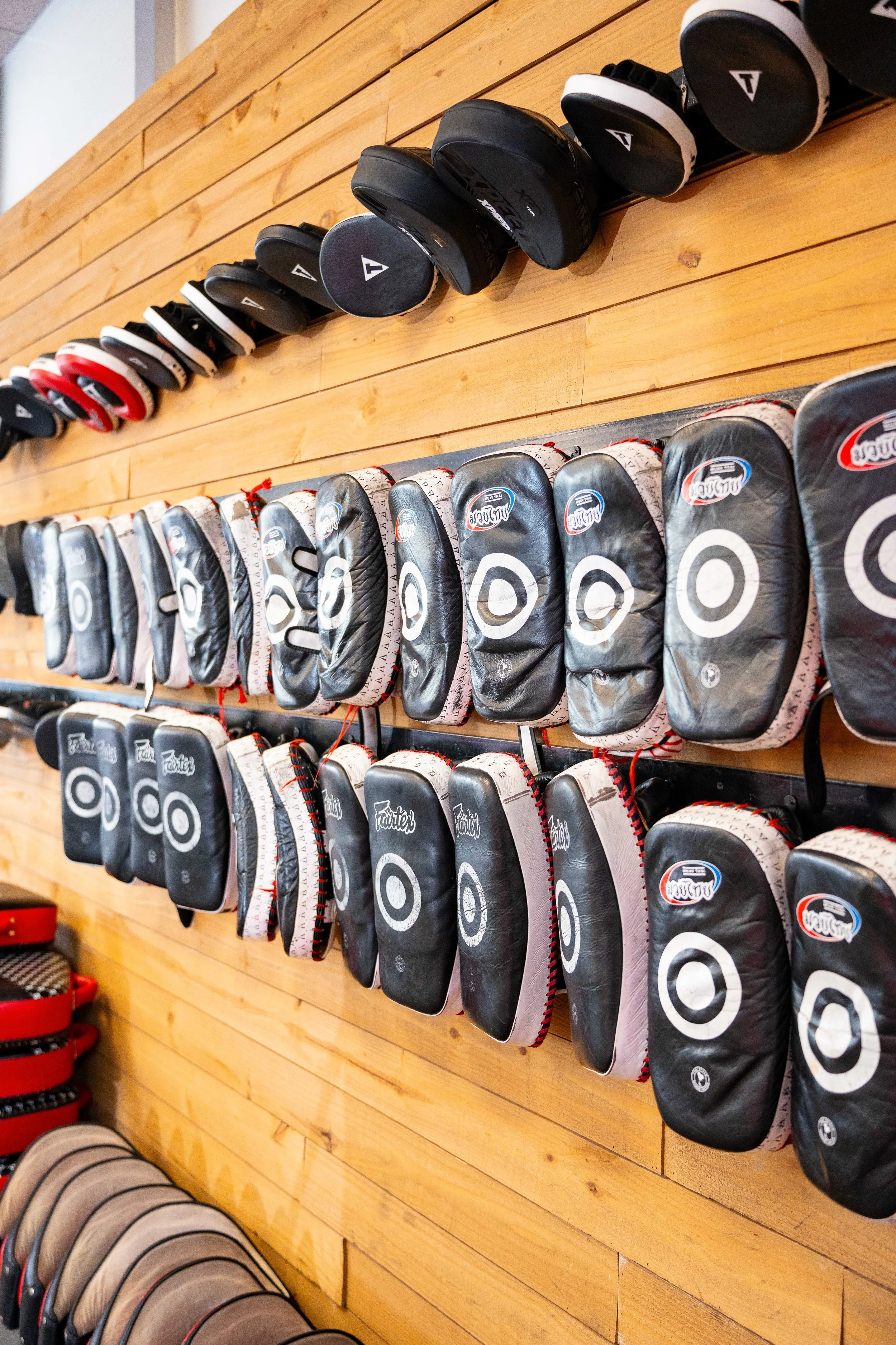 A display of various black and red hockey gloves and pads hanging on a wooden wall.