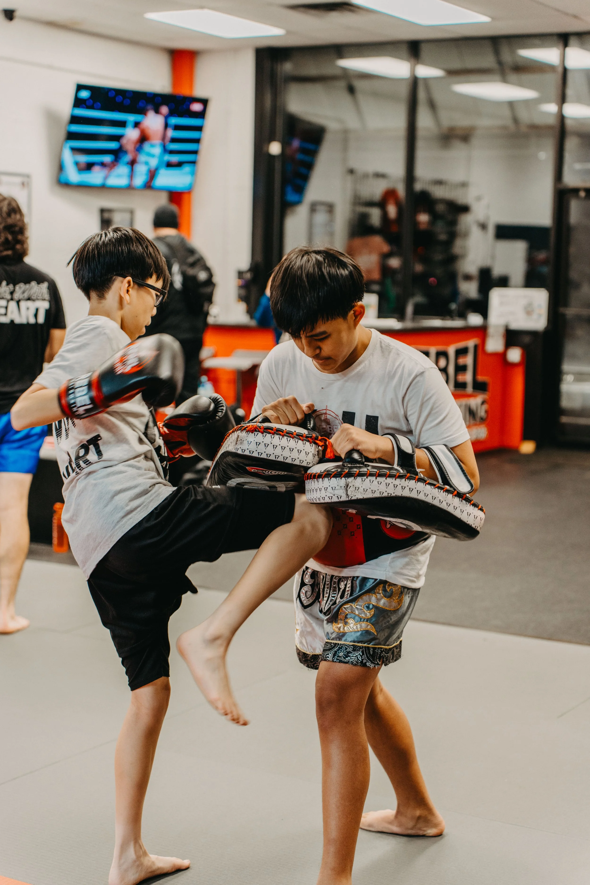 Young boys practicing martial arts with kicking shields in a gym.