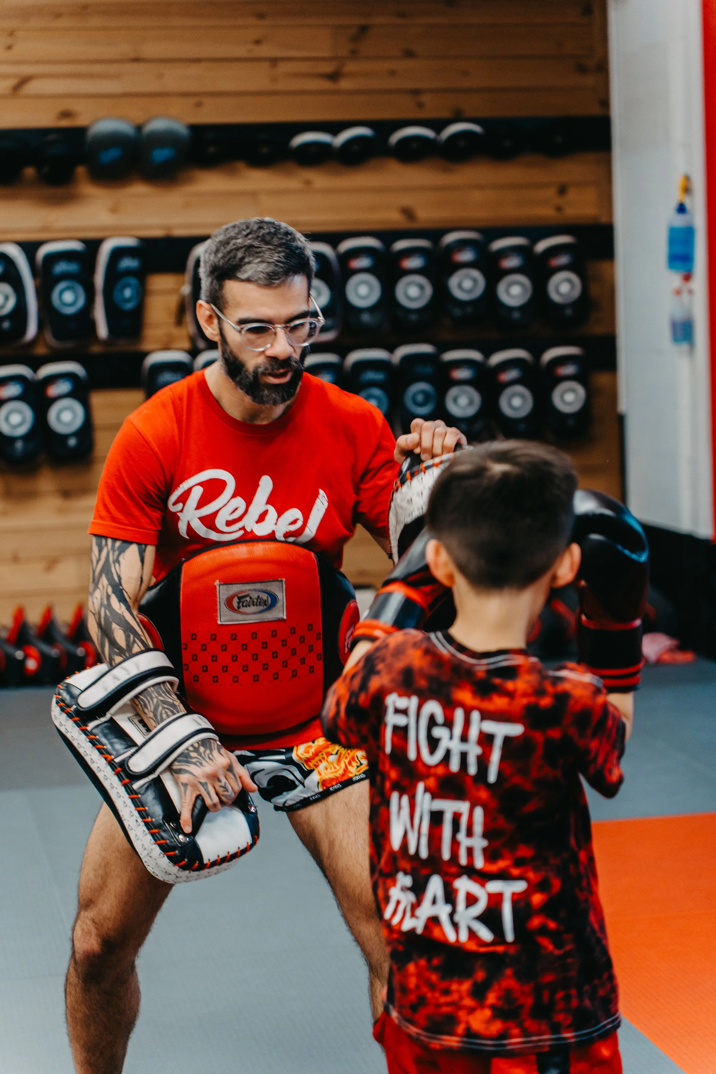 A mixed martial arts instructor and a young student practicing boxing in a gym, with boxing gloves and training gear.