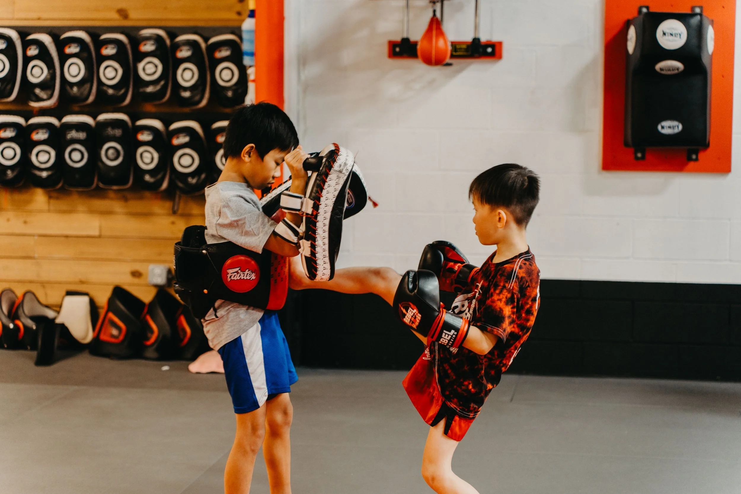 Two young boys practicing martial arts with focus, sparring in a gym, wearing boxing gloves, and training gear.
