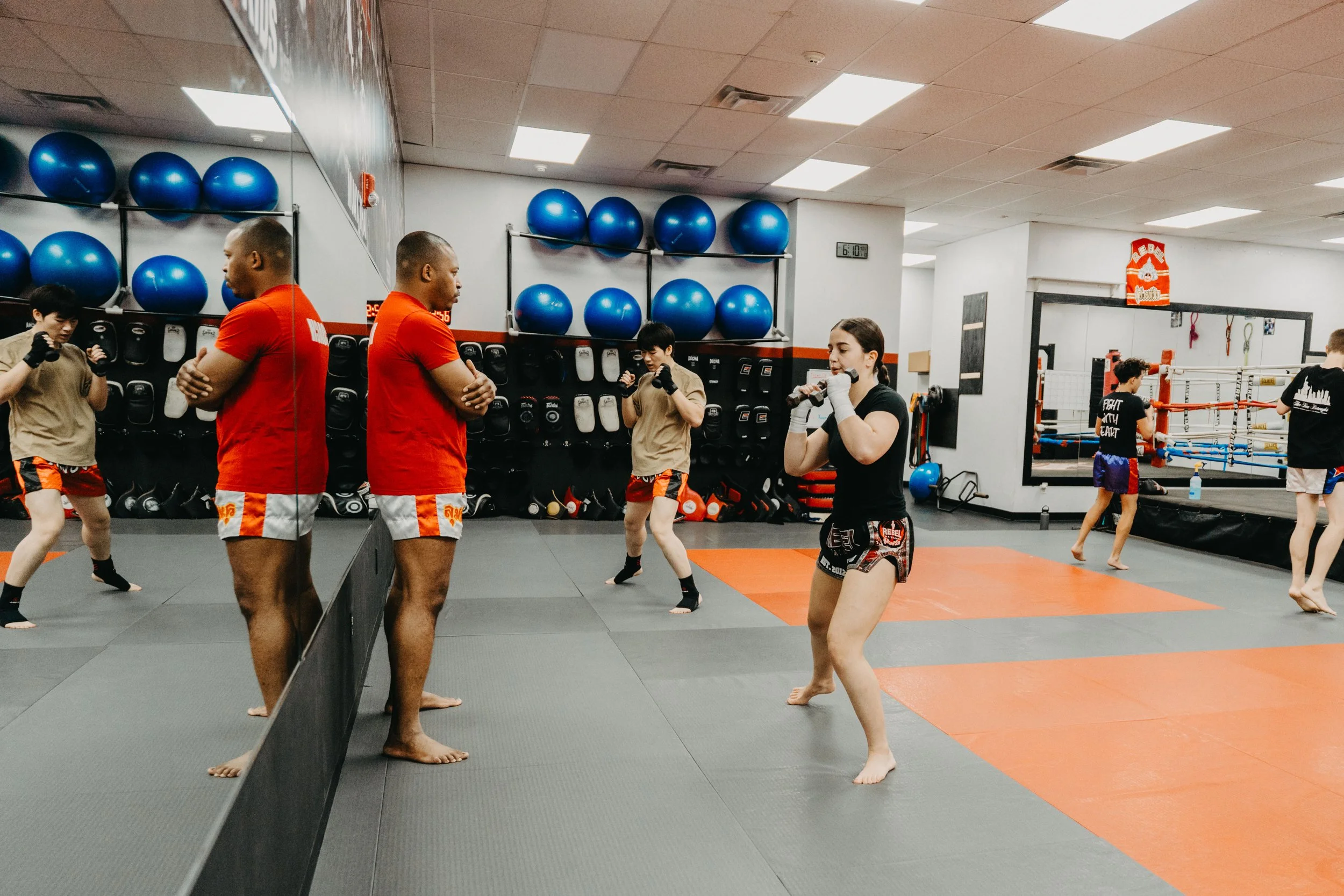 Muay Thai fighters training in a gym, practicing sparring and drills with focus mitts and pads.