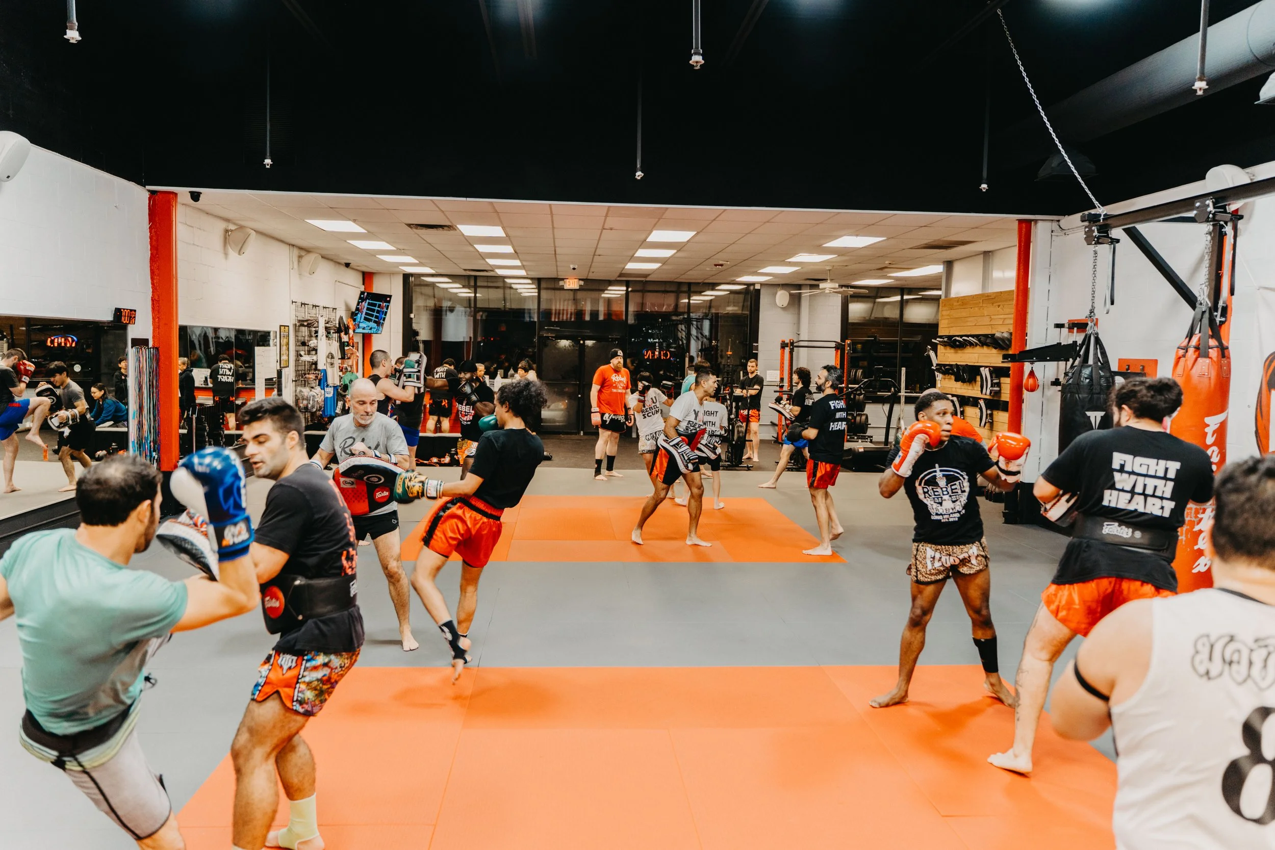 People practicing martial arts and boxing in a gym with mats, punching bags, and fitness equipment.