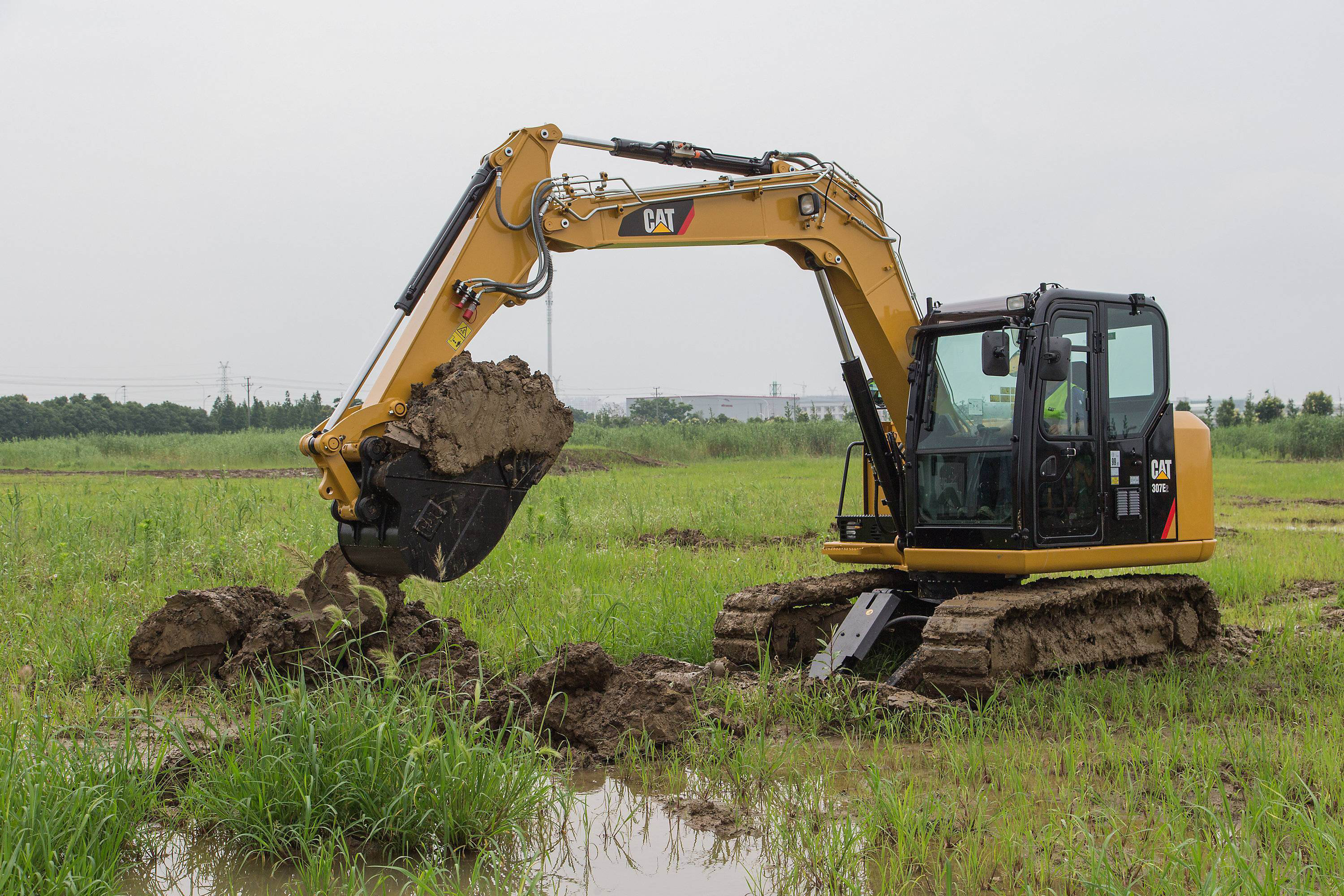 A yellow Caterpillar excavator digging in a grassy field on a cloudy day.