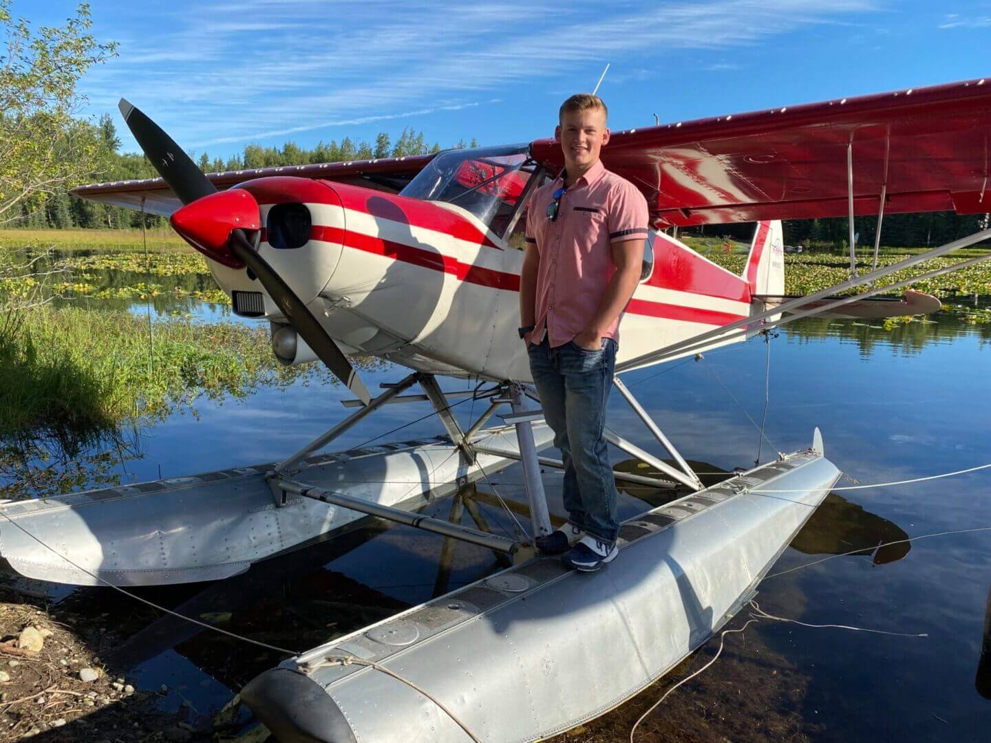 Student pilot next to red and white float plane on water during SES seaplane rating course Alaska