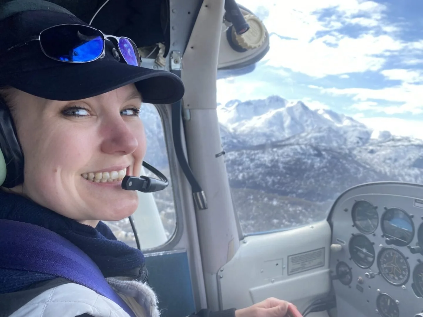 Student pilot smiling in cockpit with Alaska mountain panorama during float plane training flight
