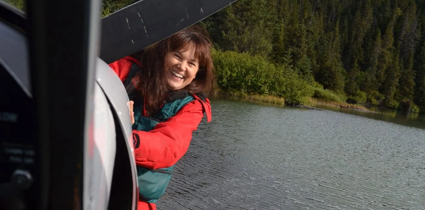Woman in red jacket standing next to float plane on scenic Alaska lake during training