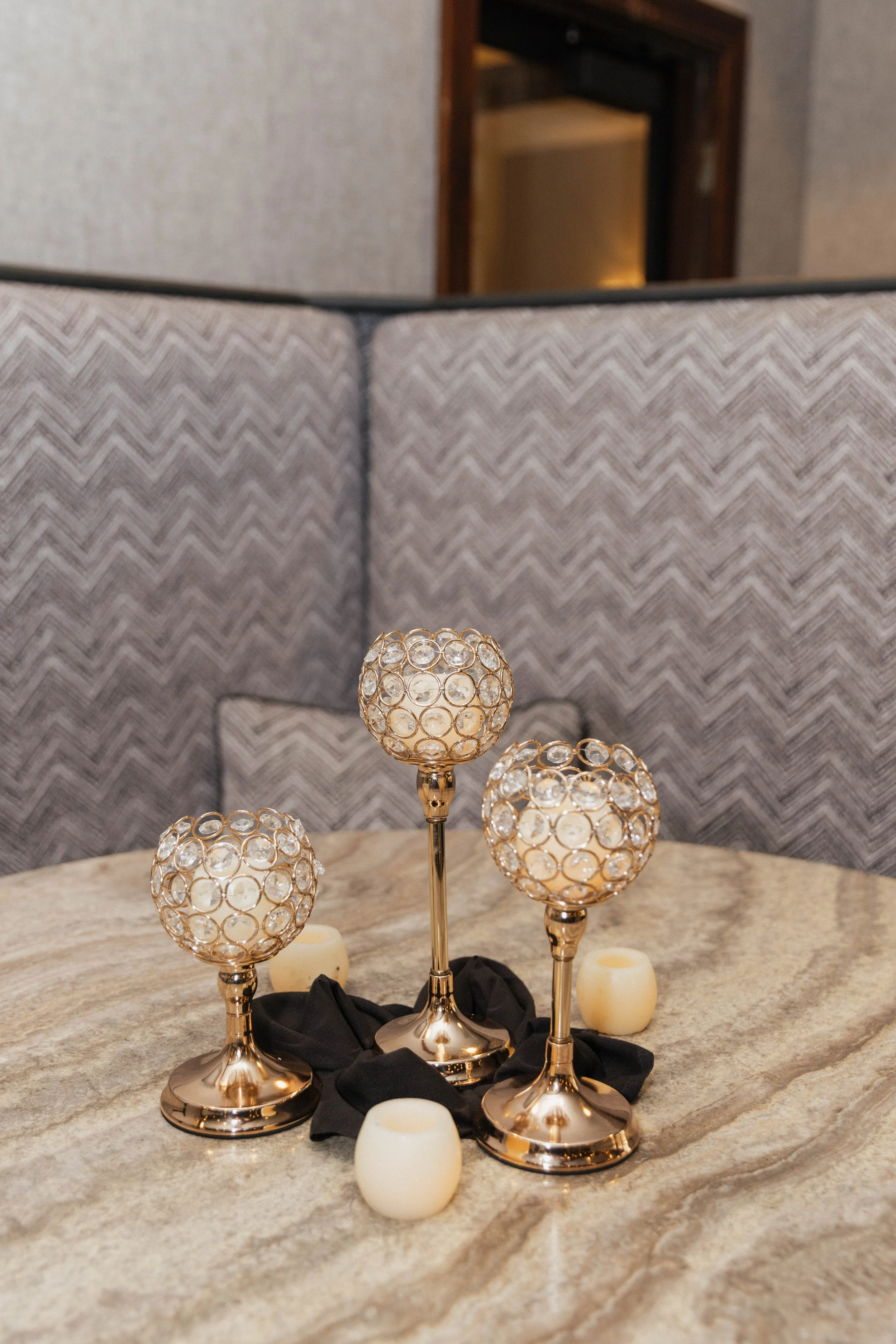 Decorative table centerpiece with three gold candle holders with glass orb tops, surrounded by four small white candle holders on a marble table.