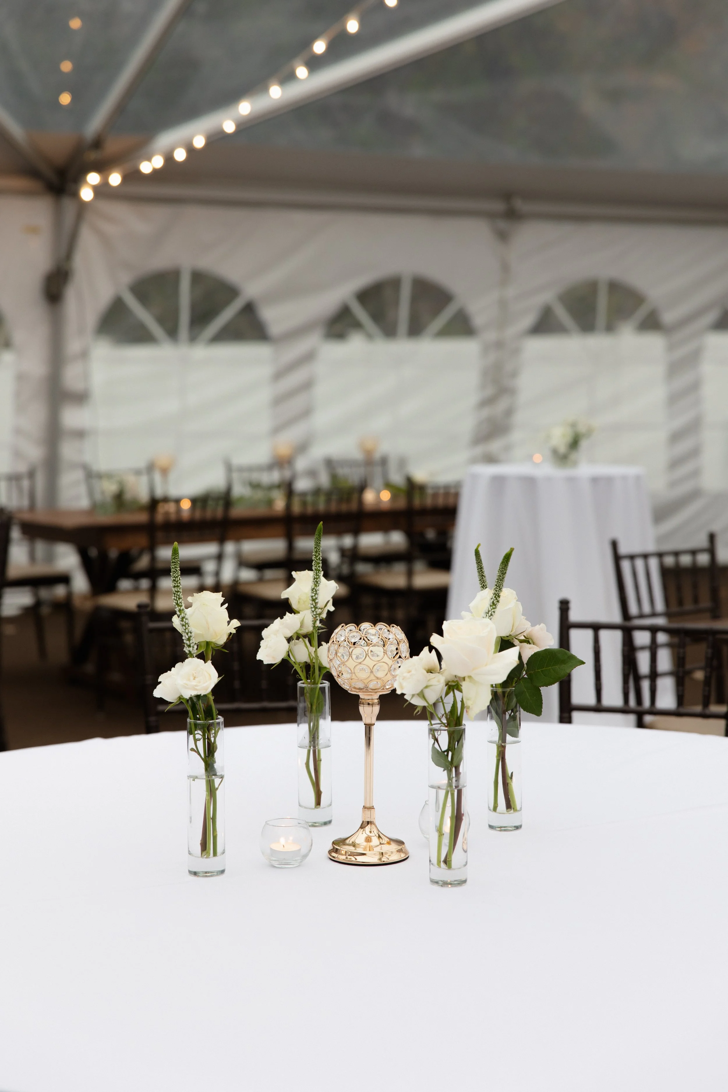 Elegant hotel lobby with cream-colored sofas, a dark wooden coffee table, floral arrangements, a staircase with wooden banisters, and a chandelier.
