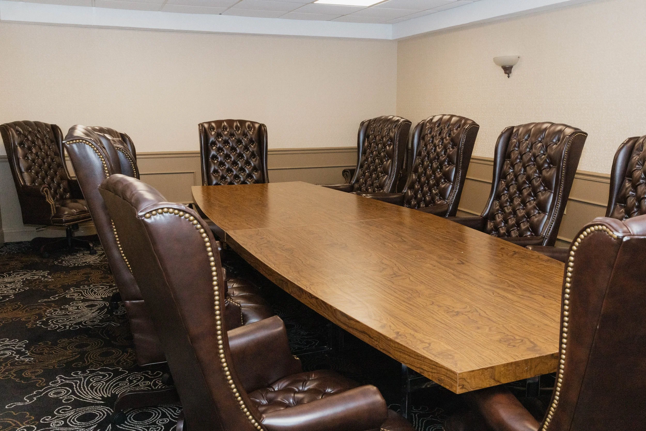 Empty conference room with a large wooden table and high-back leather chairs.
