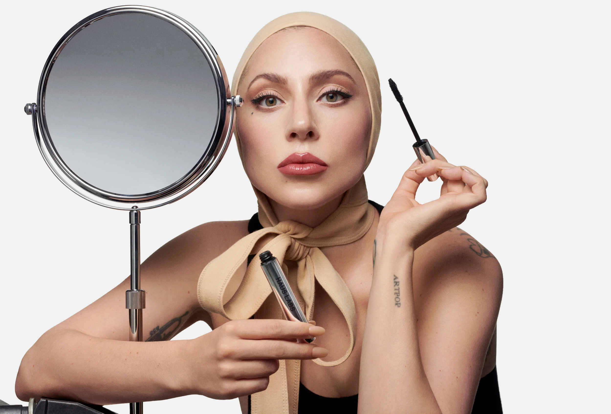 A woman applying makeup with a mascara wand while looking into a mirror.