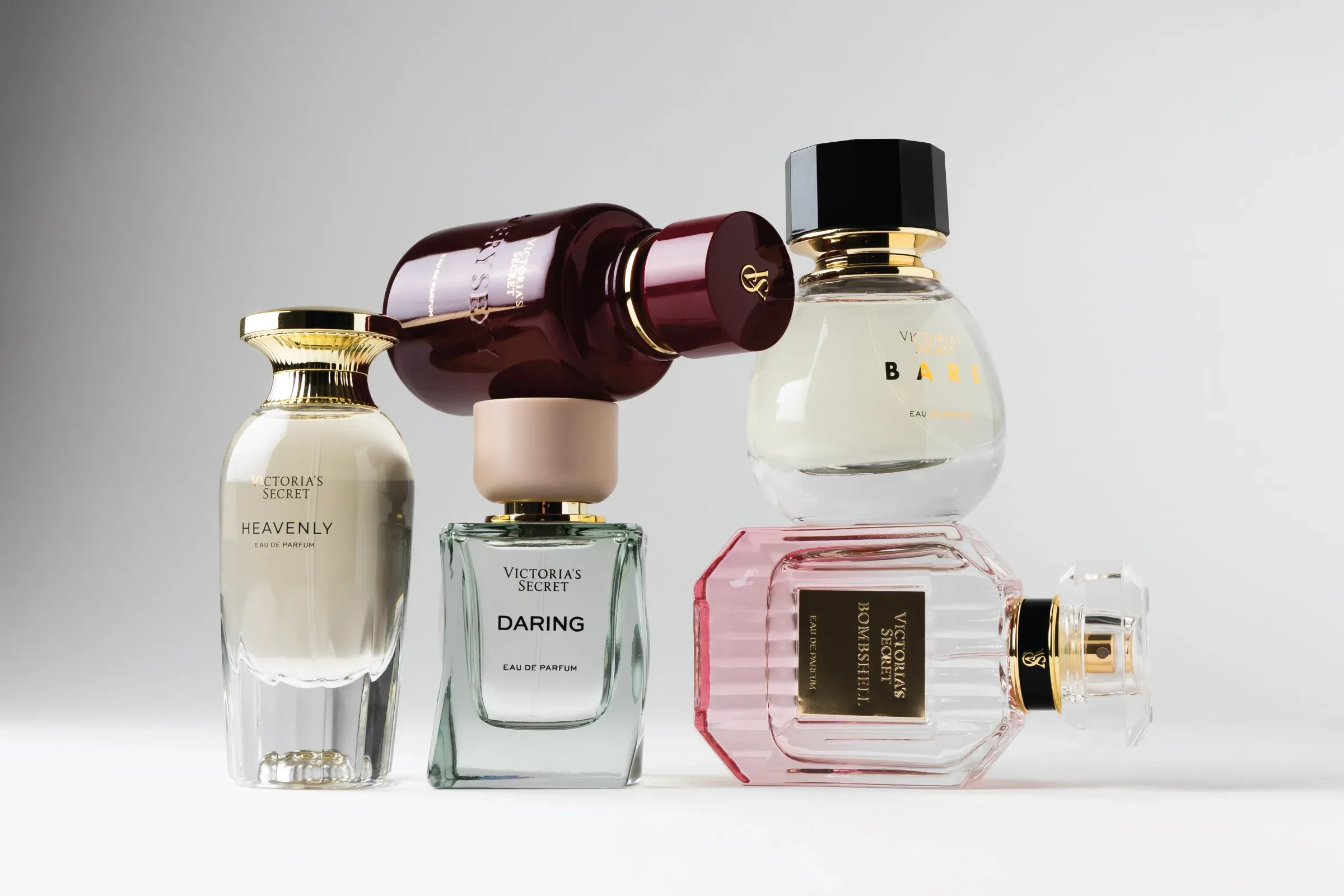 A collection of luxury perfume bottles, including Victoria's Secret Heavenly, Daring, and Bombshell, arranged on a white background.