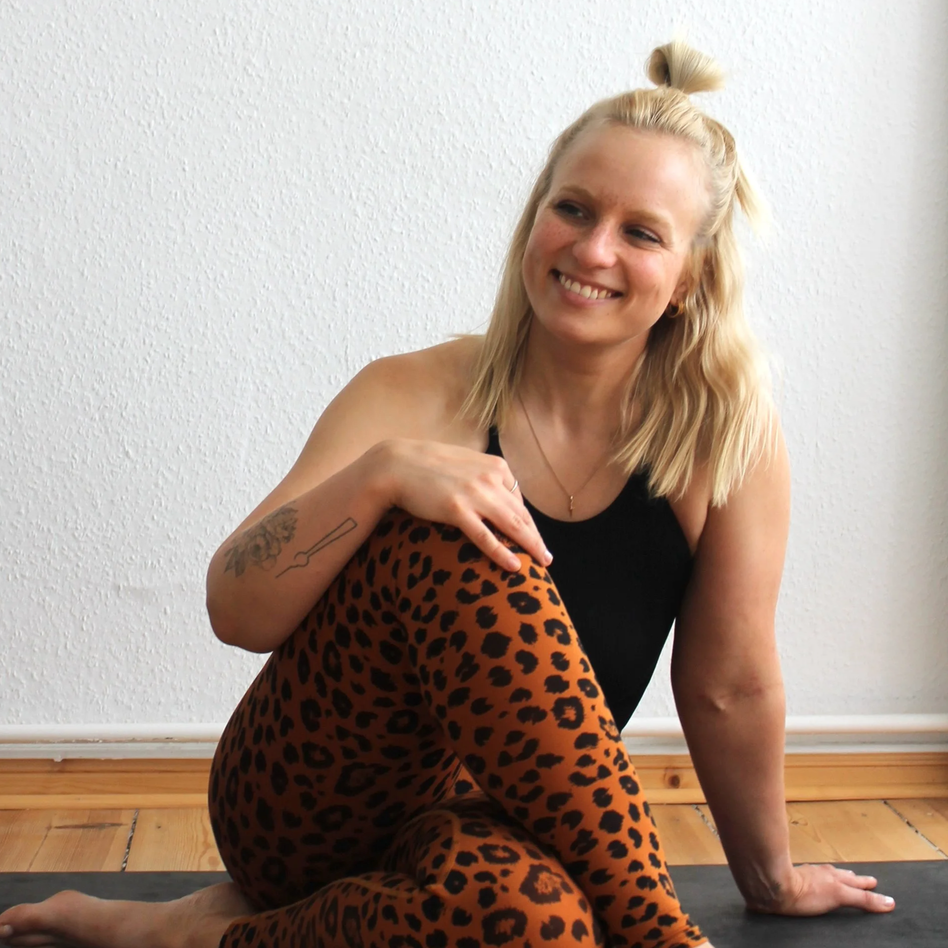 Sophie Horn, Kids-Trainerin im Mini Movers Club Berlin, sitzt lächelnd auf dem Boden eines hellen Sportstudios für Kinderkurse.