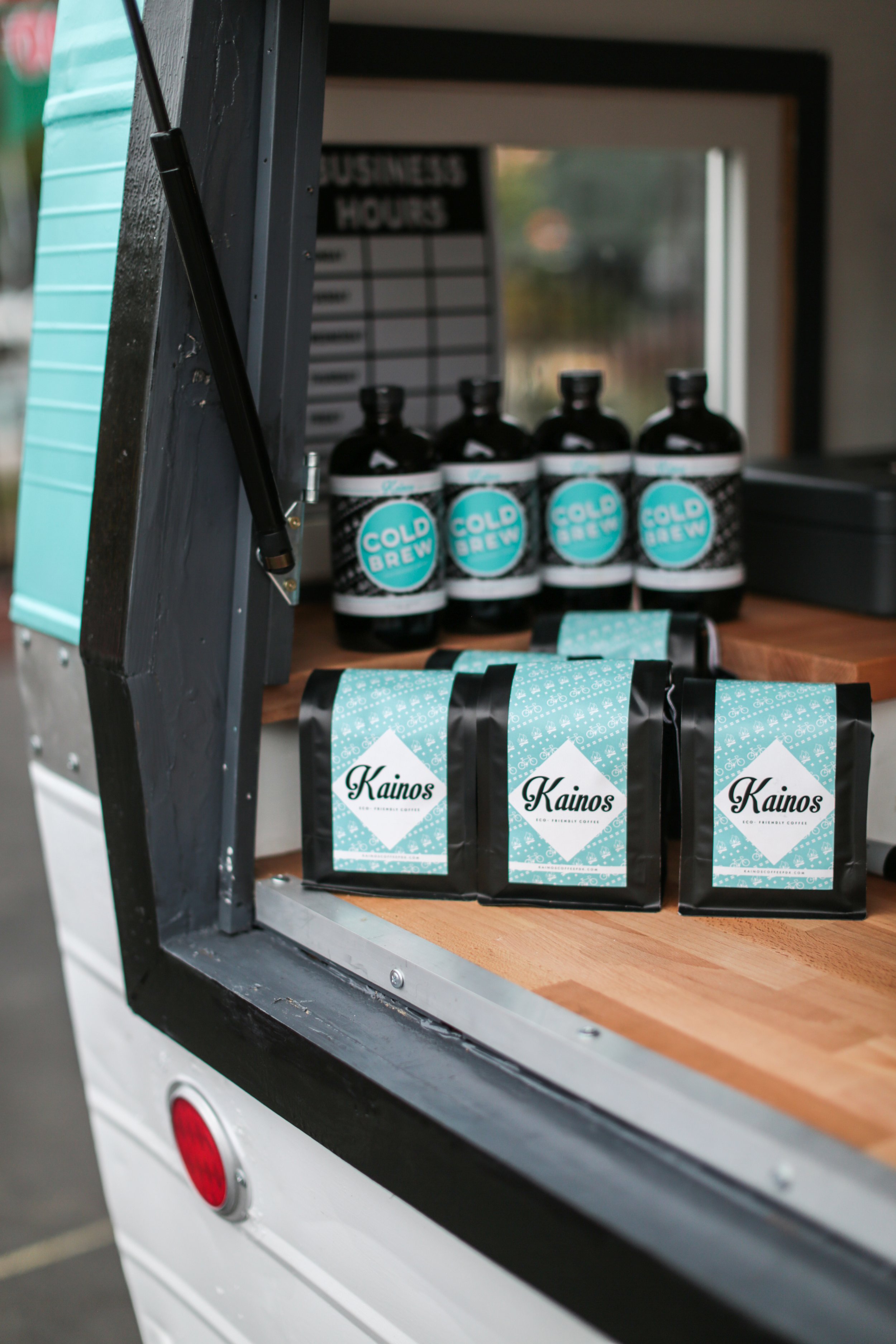 Coffee bags labeled 'Kainos' and bottles labeled 'Cold Brew' inside a coffee cart.