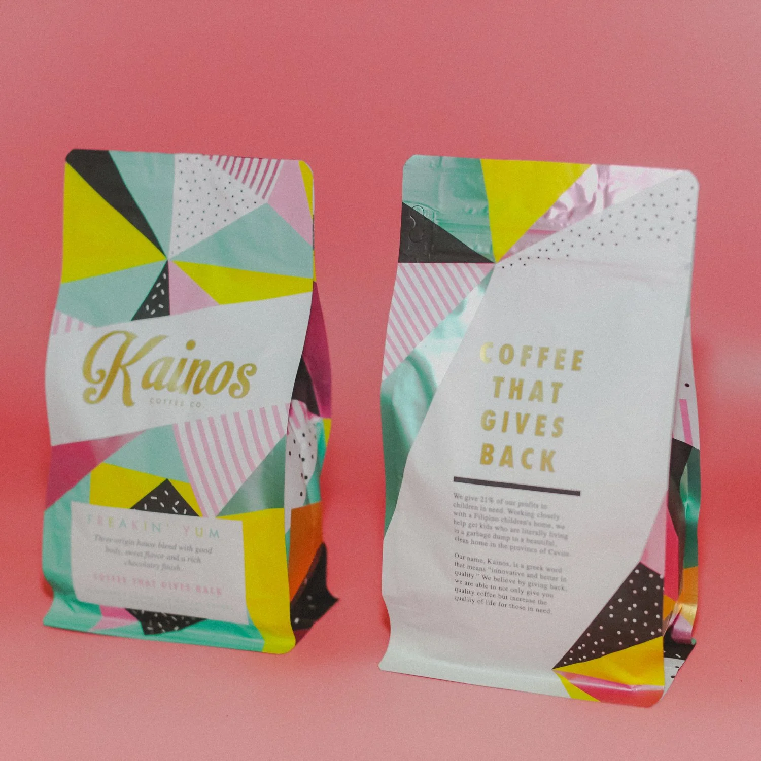 Colorful snack and coffee packaging with geometric patterns, one labeled 'Kainos' and the other with text 'Coffee that gives back' against a pink background.