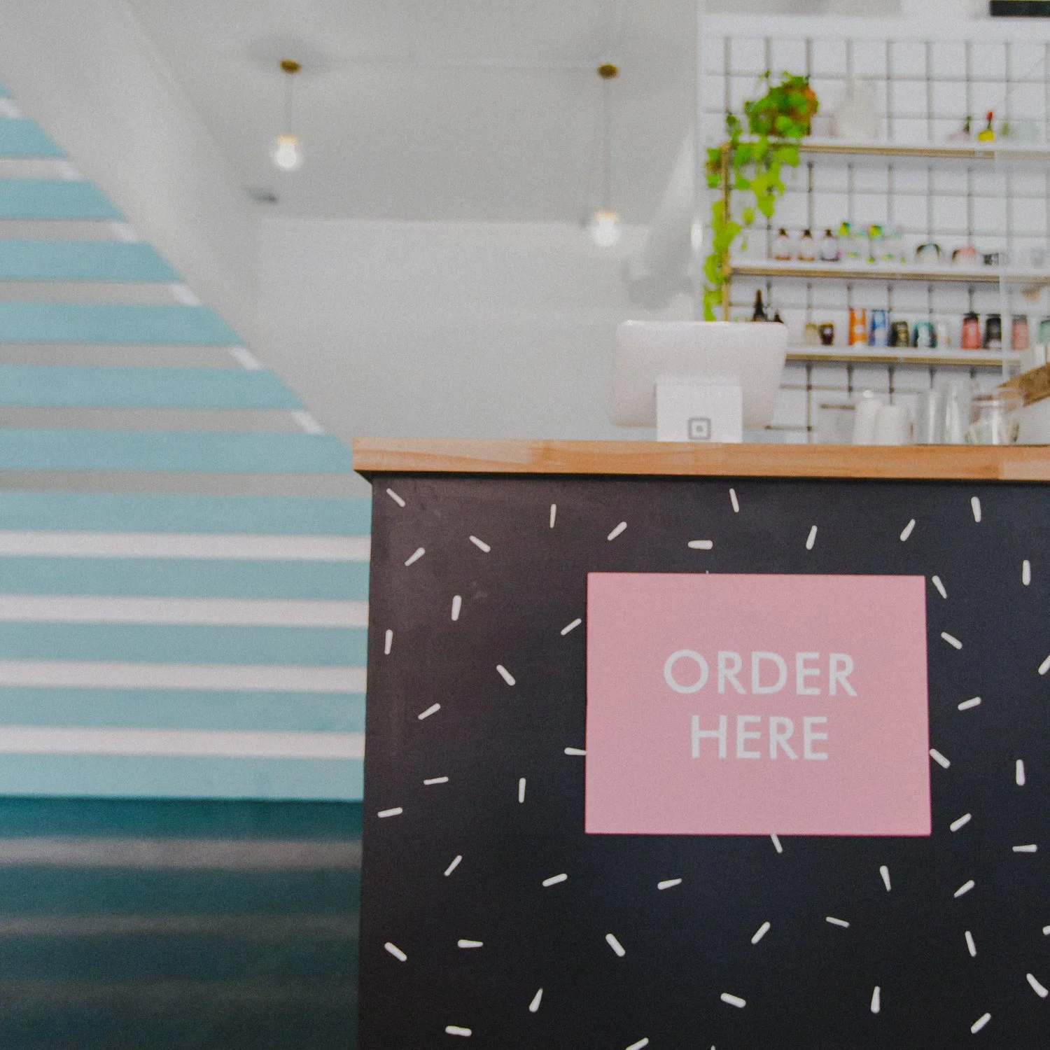 A black stand with a pink sign that says 'Order Here' in front of a modern cafe interior.