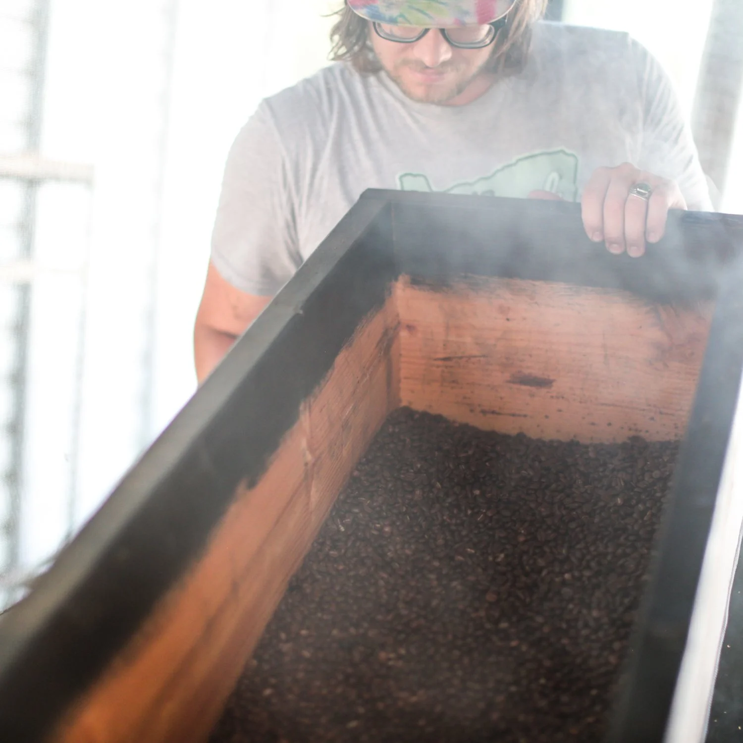 Person inspecting roasted coffee beans in a wooden roaster.