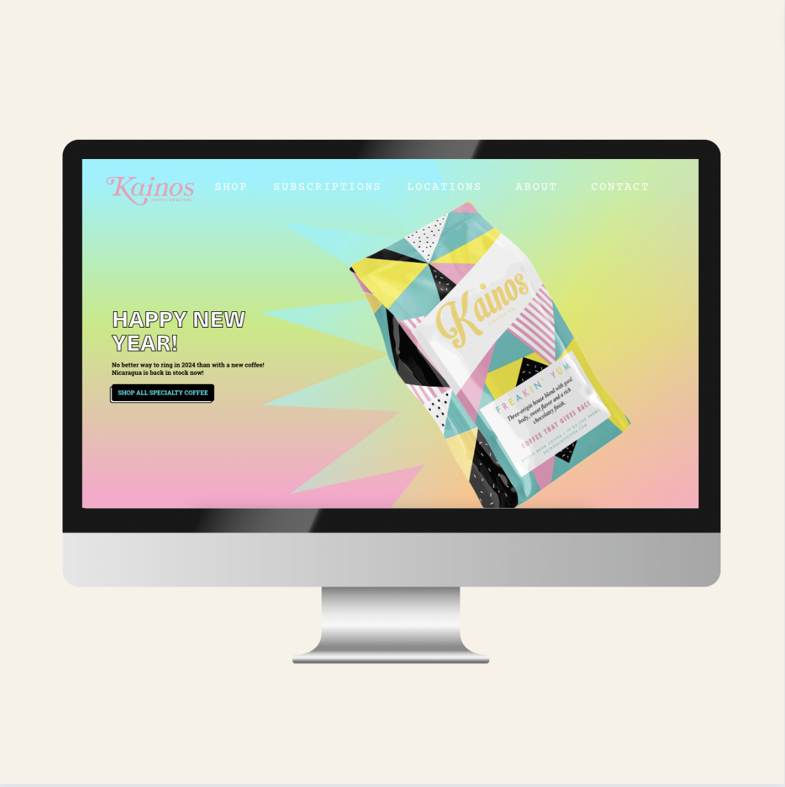Computer monitor displaying a colorful website for Kainos coffee, with a New Year's greeting and a 3D coffee package design on the screen.