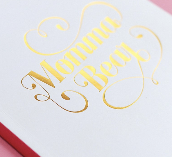 Gold foil stamped text reading 'Momma Beauty' on a white surface with a pink border.