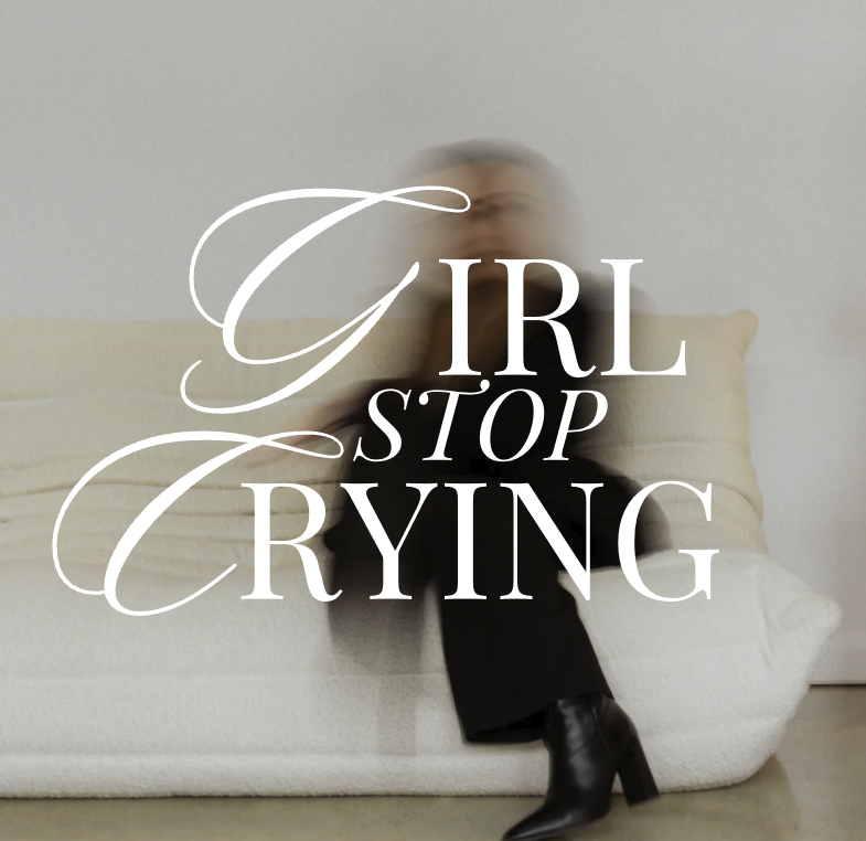 A woman sitting on a beige couch, with a message overlayed that says 'Girl, stop crying'.