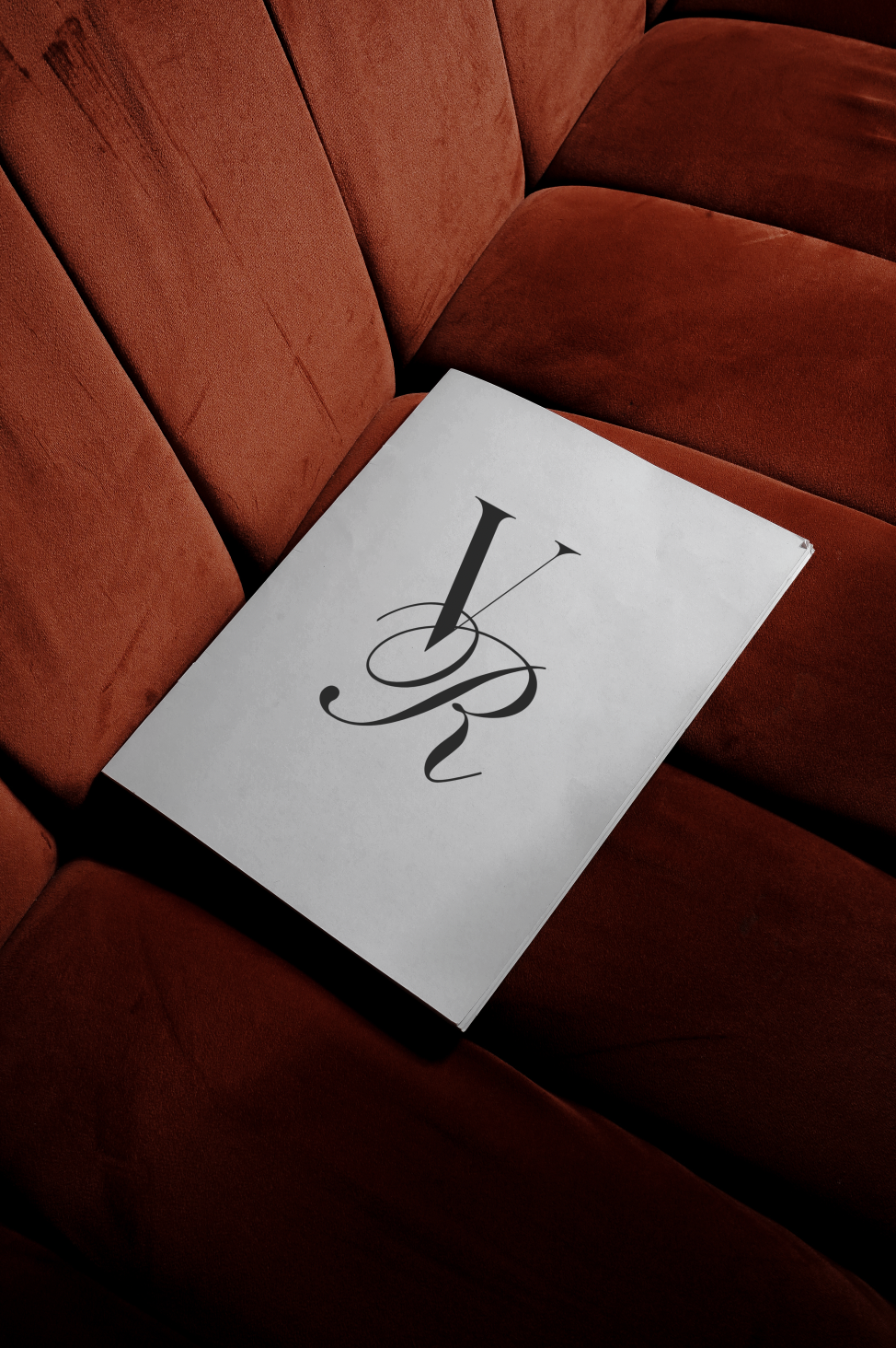 A paper with a stylized black letter 'L' on a white background, resting on a red upholstered couch.