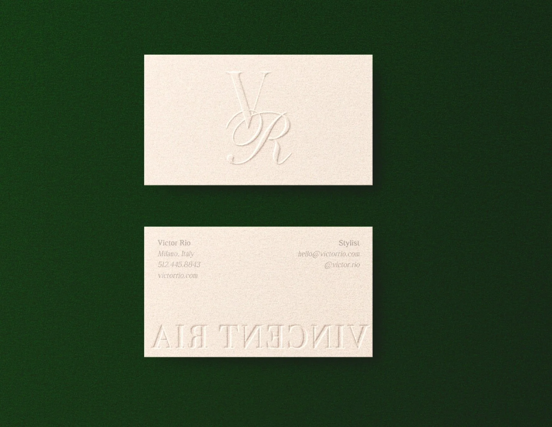 A minimalistic business card with embossed logo and textured cream background, placed on a dark green surface.