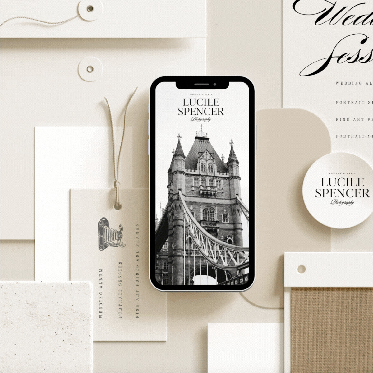 A black-and-white photo of Tower Bridge on a smartphone screen, surrounded by branding materials for Lucile Spencer Photography, including cards, tags, and sample swatches in a neutral color palette.