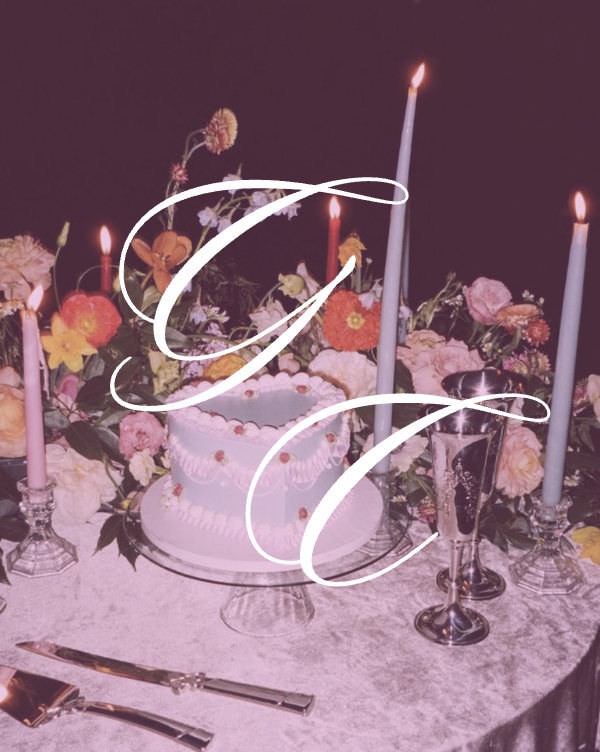 Decorative cake with flowers, candles, and champagne glasses on a table at a celebration or party.