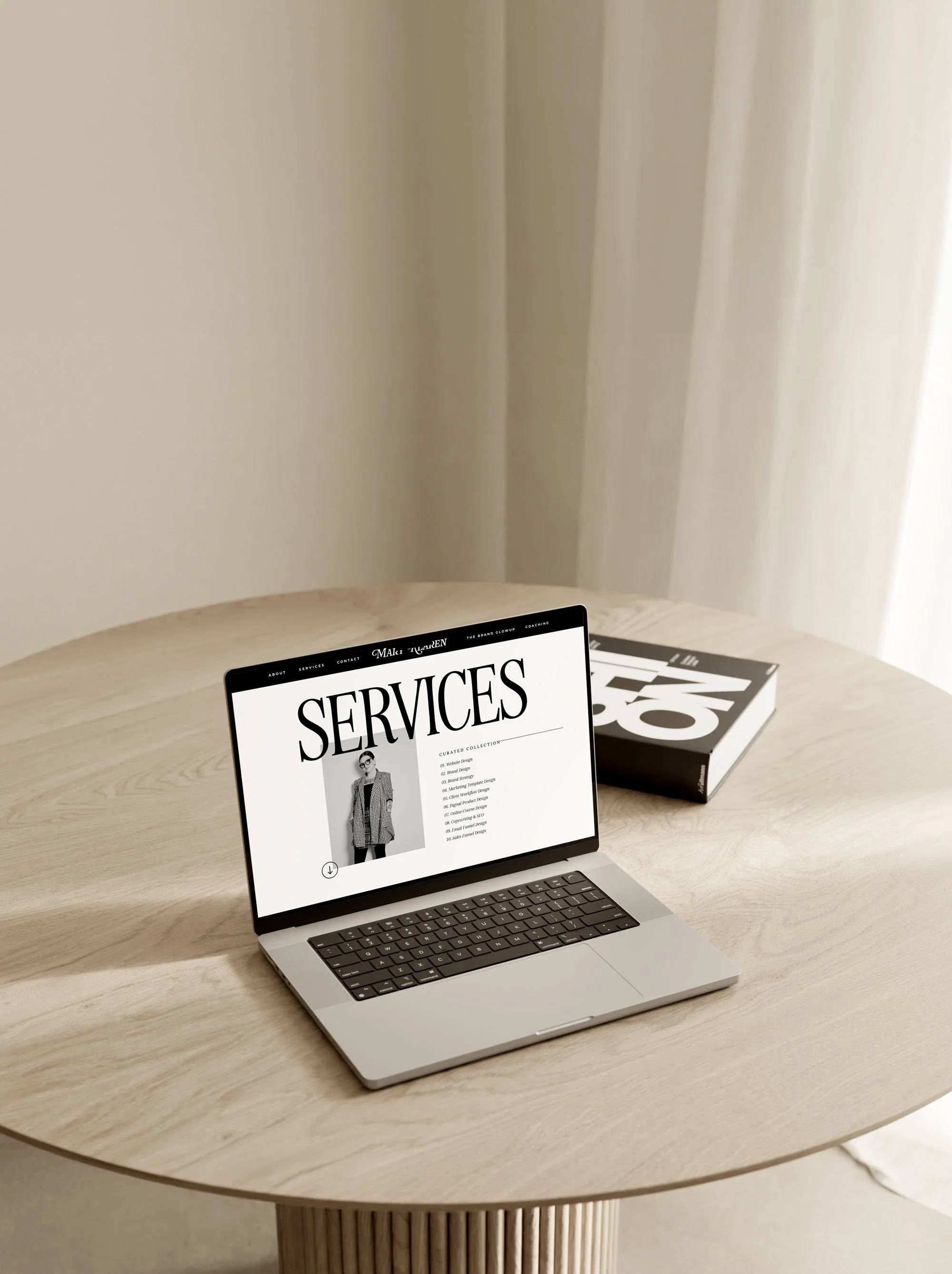 Laptop on a wooden table displaying a webpage titled 'Services' with an image of a woman in a coat, next to a large, black and white book.