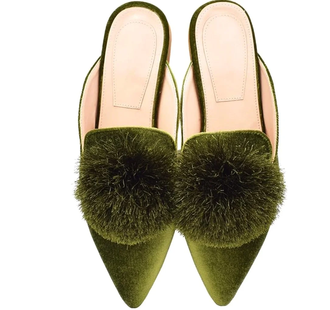 Pair of green velvet pointed-toe slippers with fluffy pom-pom embellishments on the front.