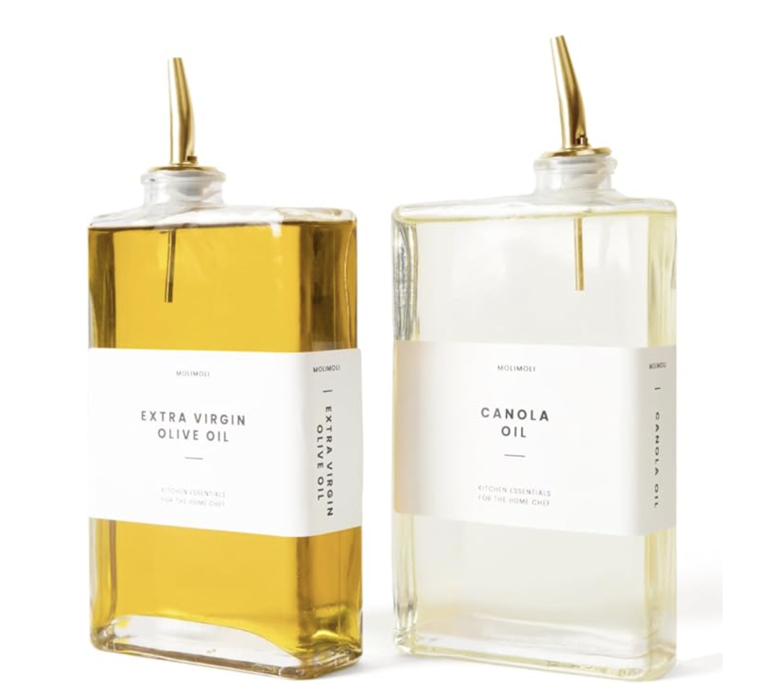 Two glass bottles of cooking oil, one extra virgin olive oil on the left and one canola oil on the right, with labels and golden dispensing spouts.