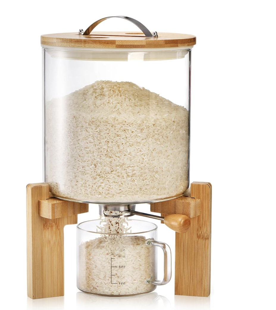 A glass rice dispenser with a bamboo lid and wooden stand, dispensing rice into a glass measuring cup.