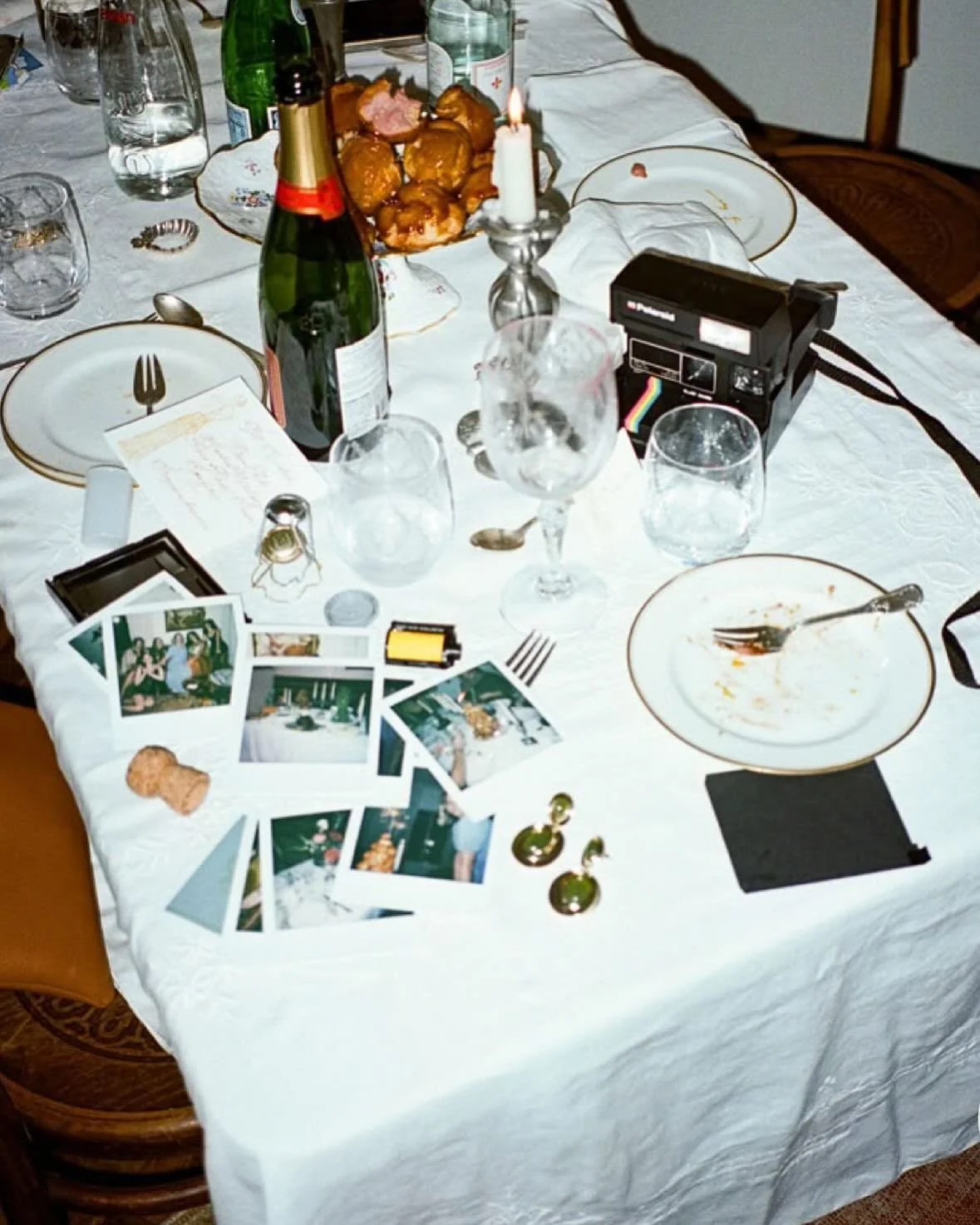 A dining table with empty and partially eaten plates, glasses, bottles, photos, and a lit candle.
