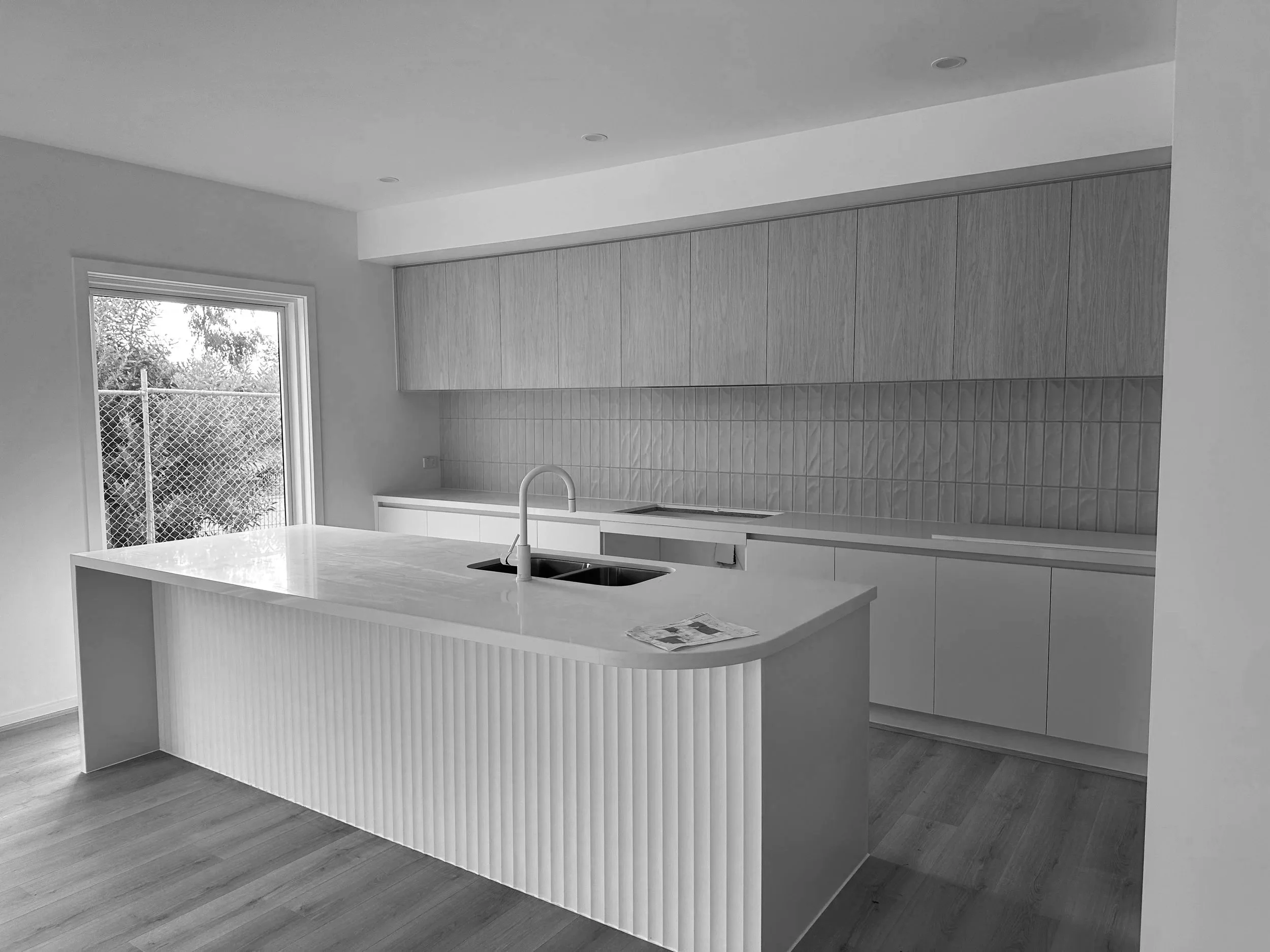Modern kitchen with a large island, double sink, wood cabinets, tiled backsplash, and a sliding glass door to the outside.