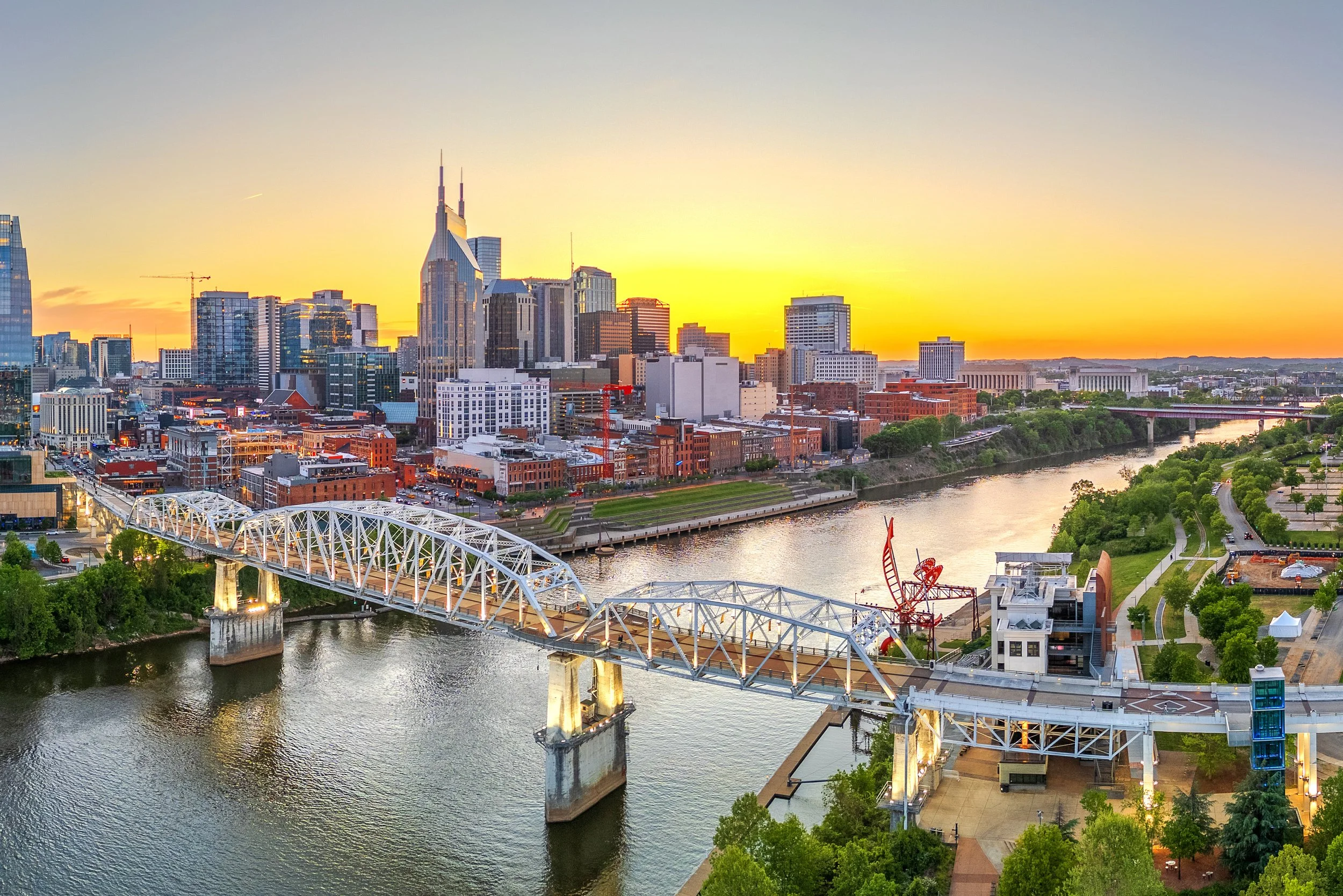 A city skyline at sunset with a river and a bridge in the foreground, and high-rise buildings in the background.