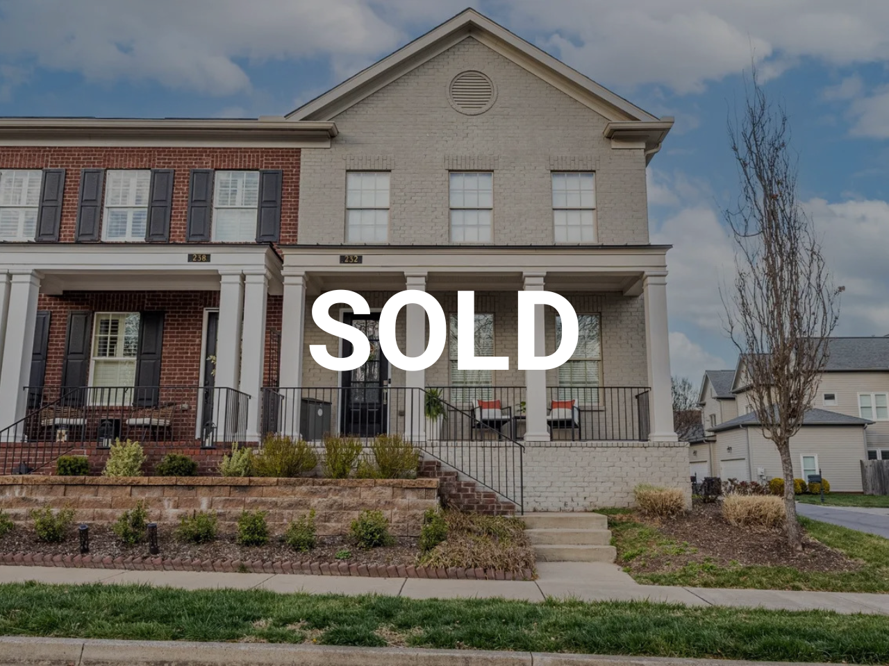 Two-story house with a front porch, attached to a red-brick house on the left, and a yard with shrubs and a sidewalk in front. The house has the number 232 and is marked as sold.