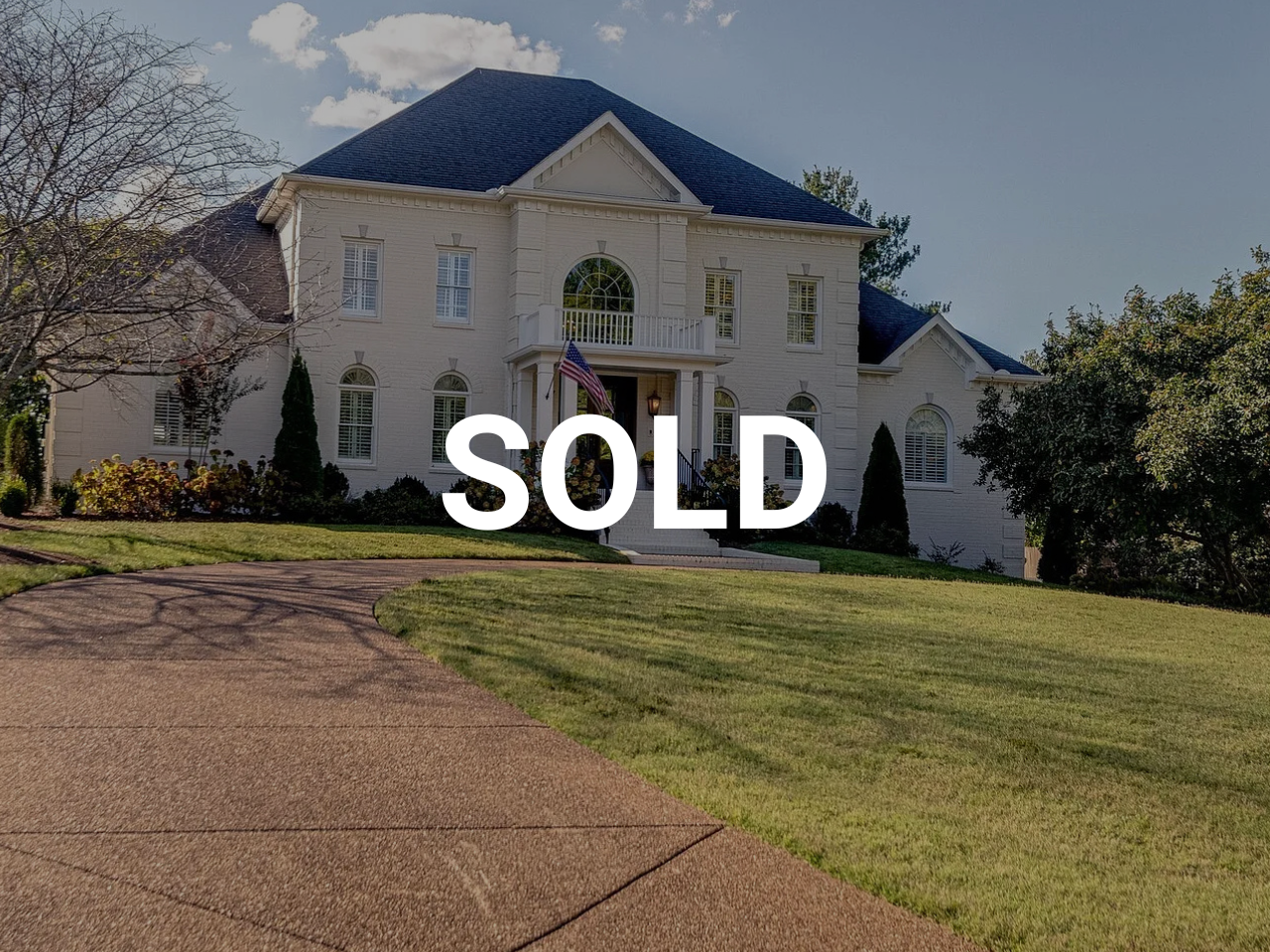 Large white house with a dark roof, surrounded by trees and a landscaped lawn, with a driveway in the foreground. The word "SOLD" is overlaid in white text.