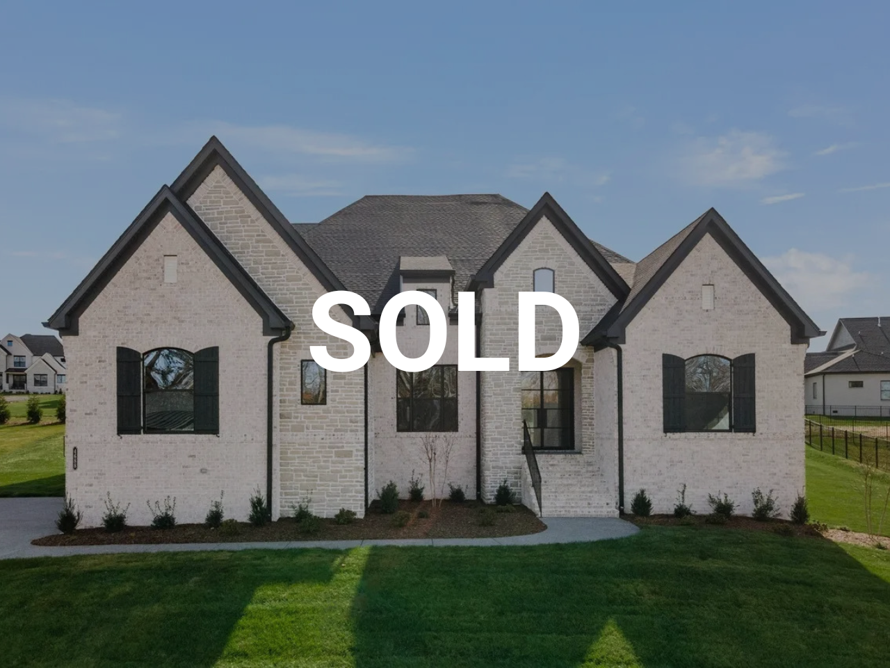 Front of a sold two-story house with gray brick walls, black shutters, and a well-maintained lawn.